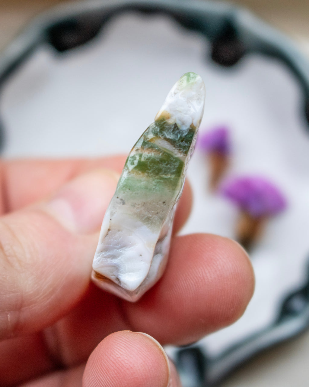 Hand holding a green and white stone with a blurred background