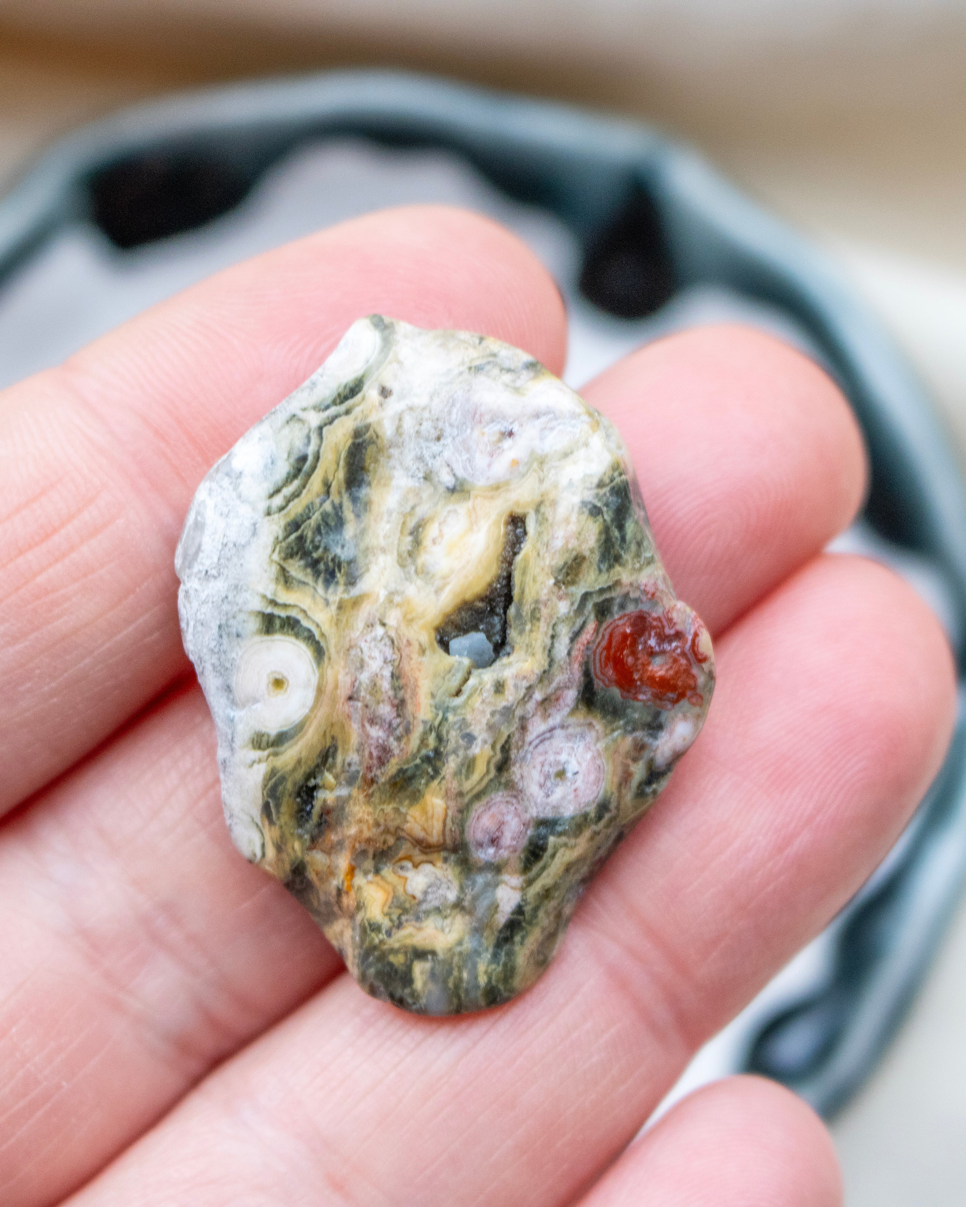 Hand holding a rough, multicolored stone with a blurred background