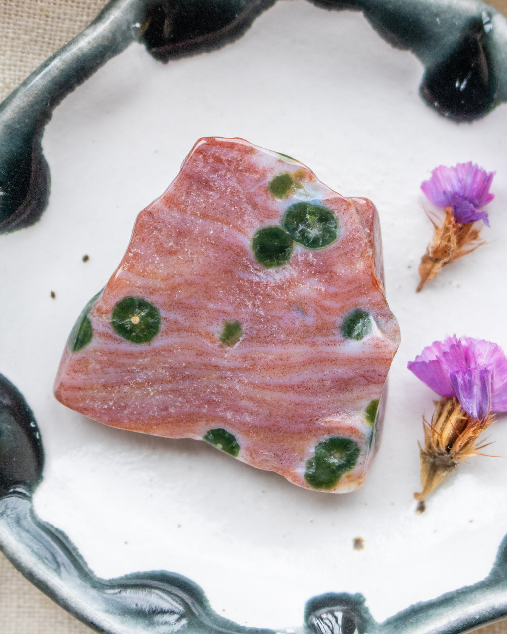 a red and green patterned stone on a ceramic plate with purple flowers