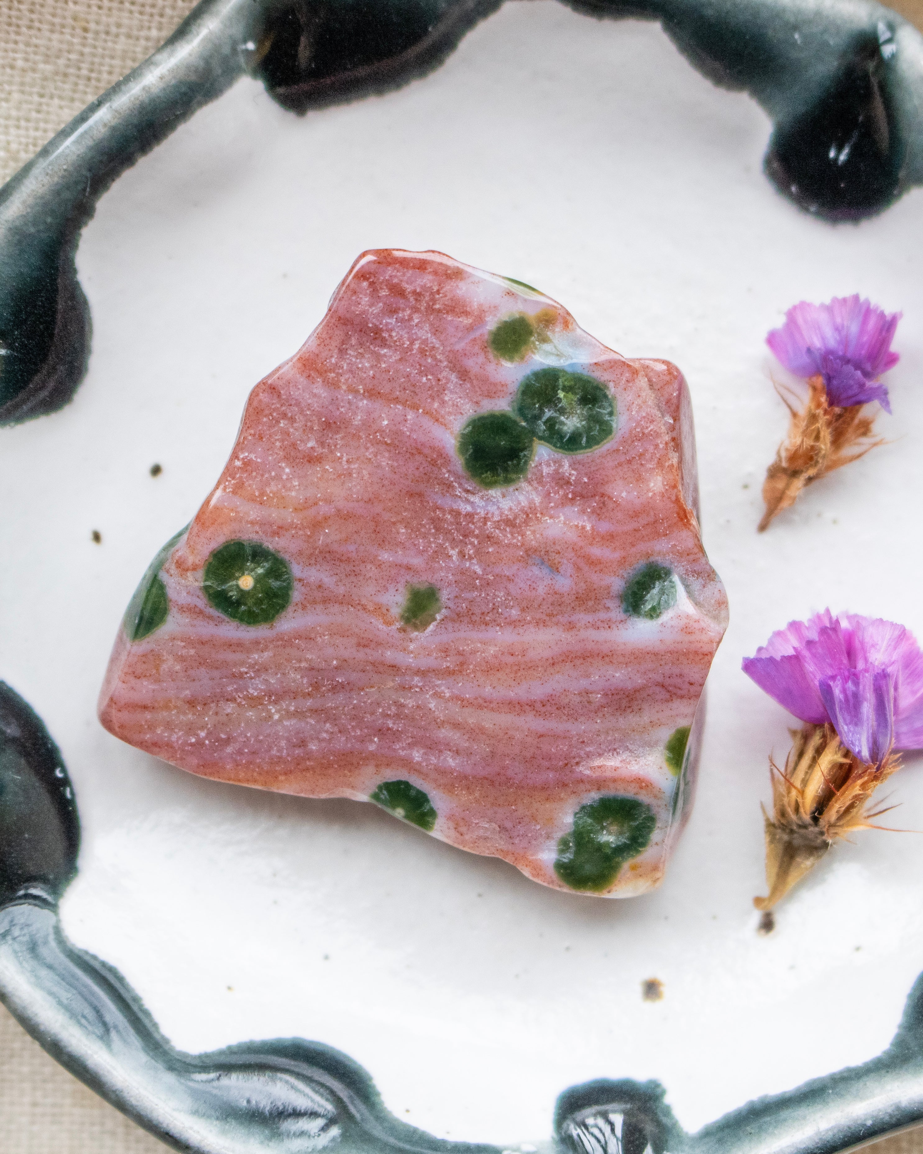 a red and green patterned stone on a ceramic plate with purple flowers