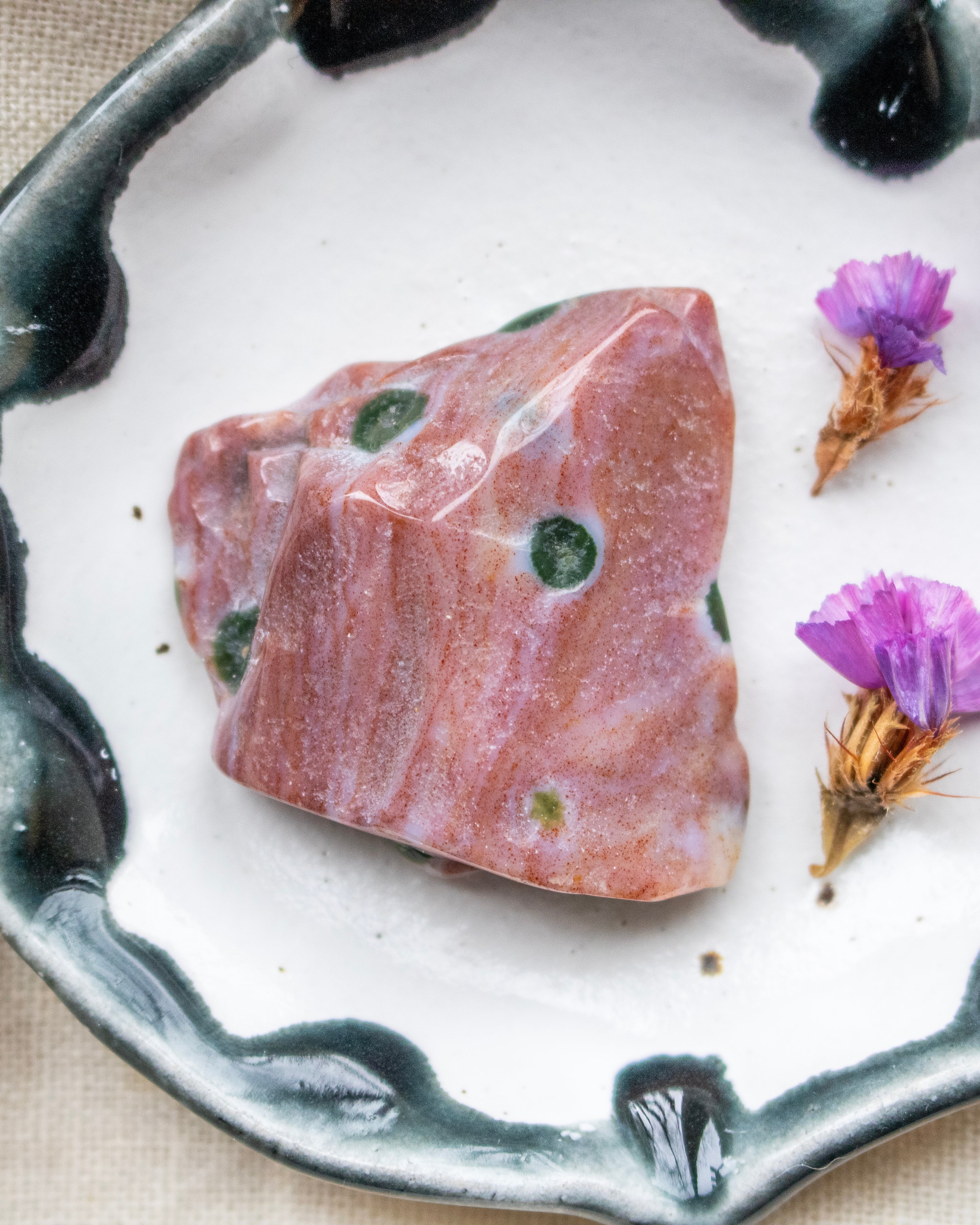 a red and green patterned stone on a ceramic plate with purple flowers