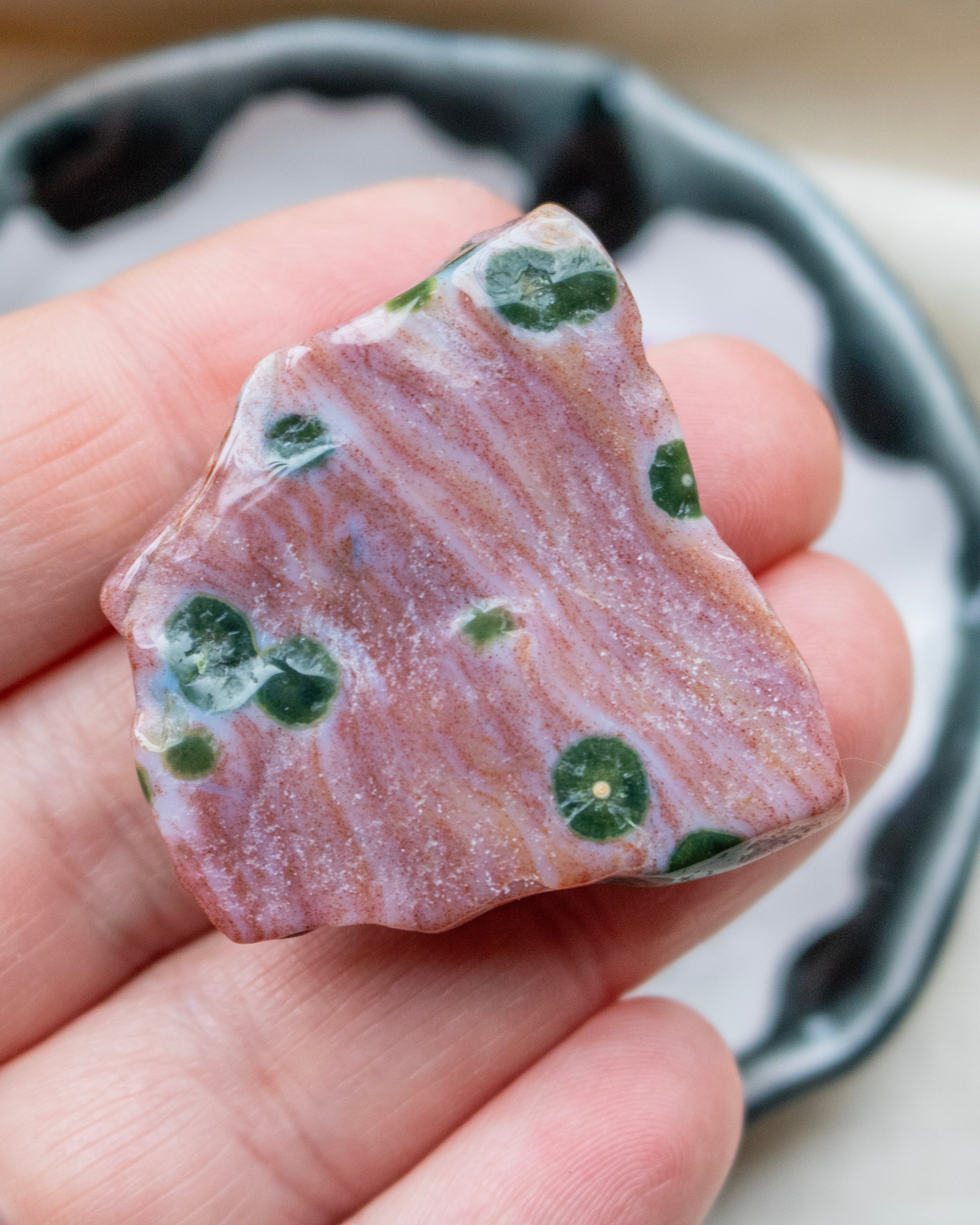 Polished stone with green spots held in a hand against a neutral background