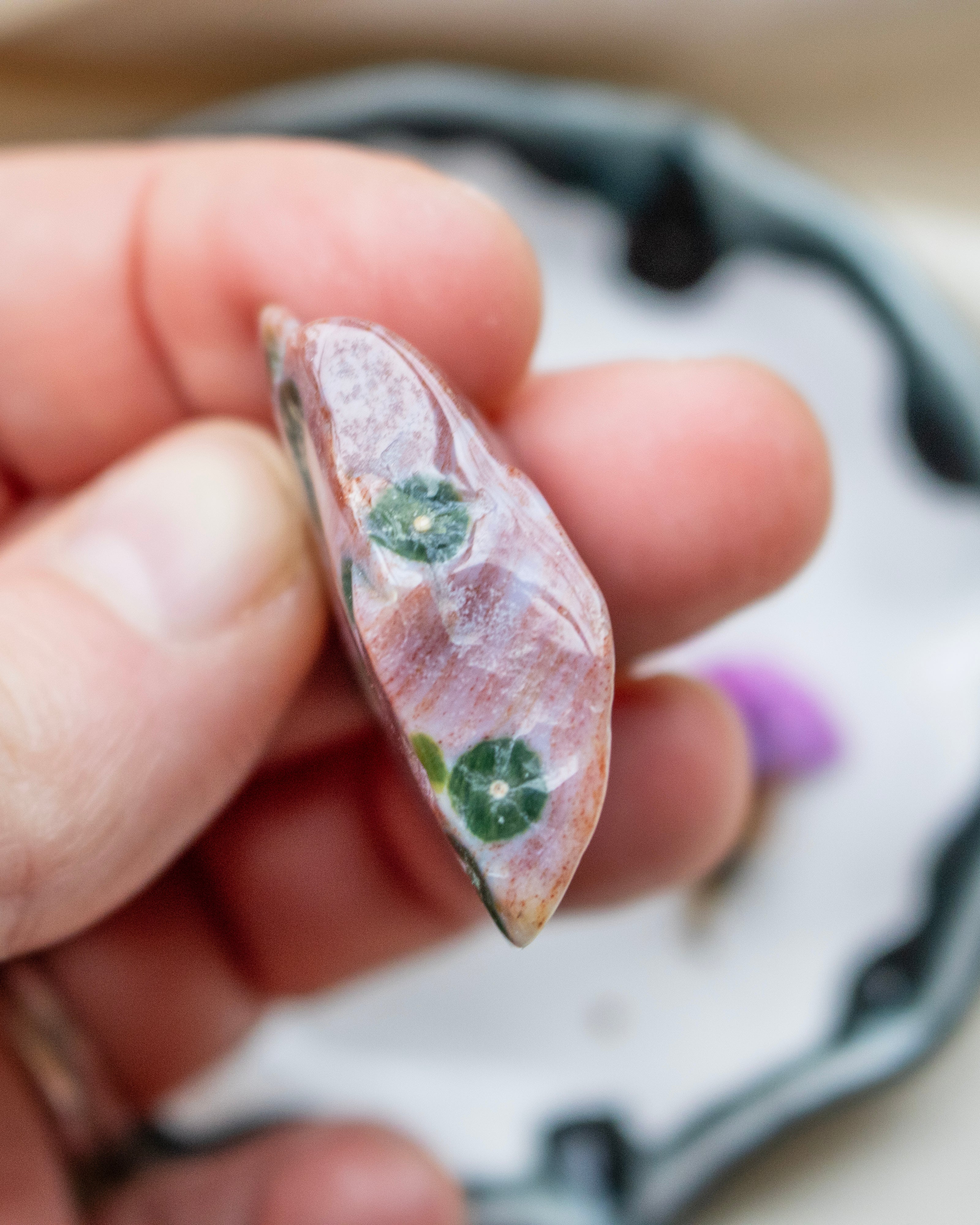 Pink stone with green inclusions held between fingers against a blurred background