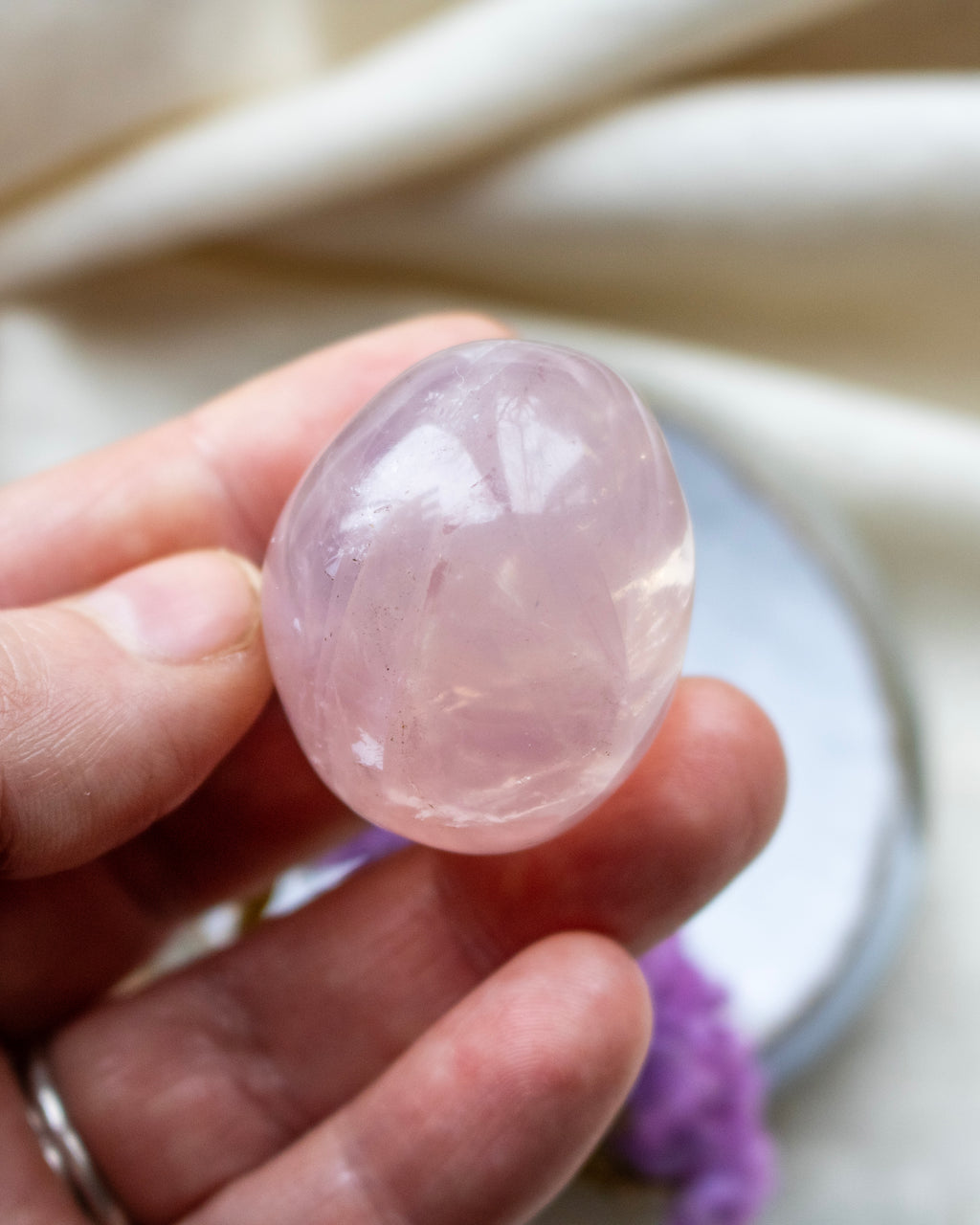 Hand holding a pink crystal against a neutral background