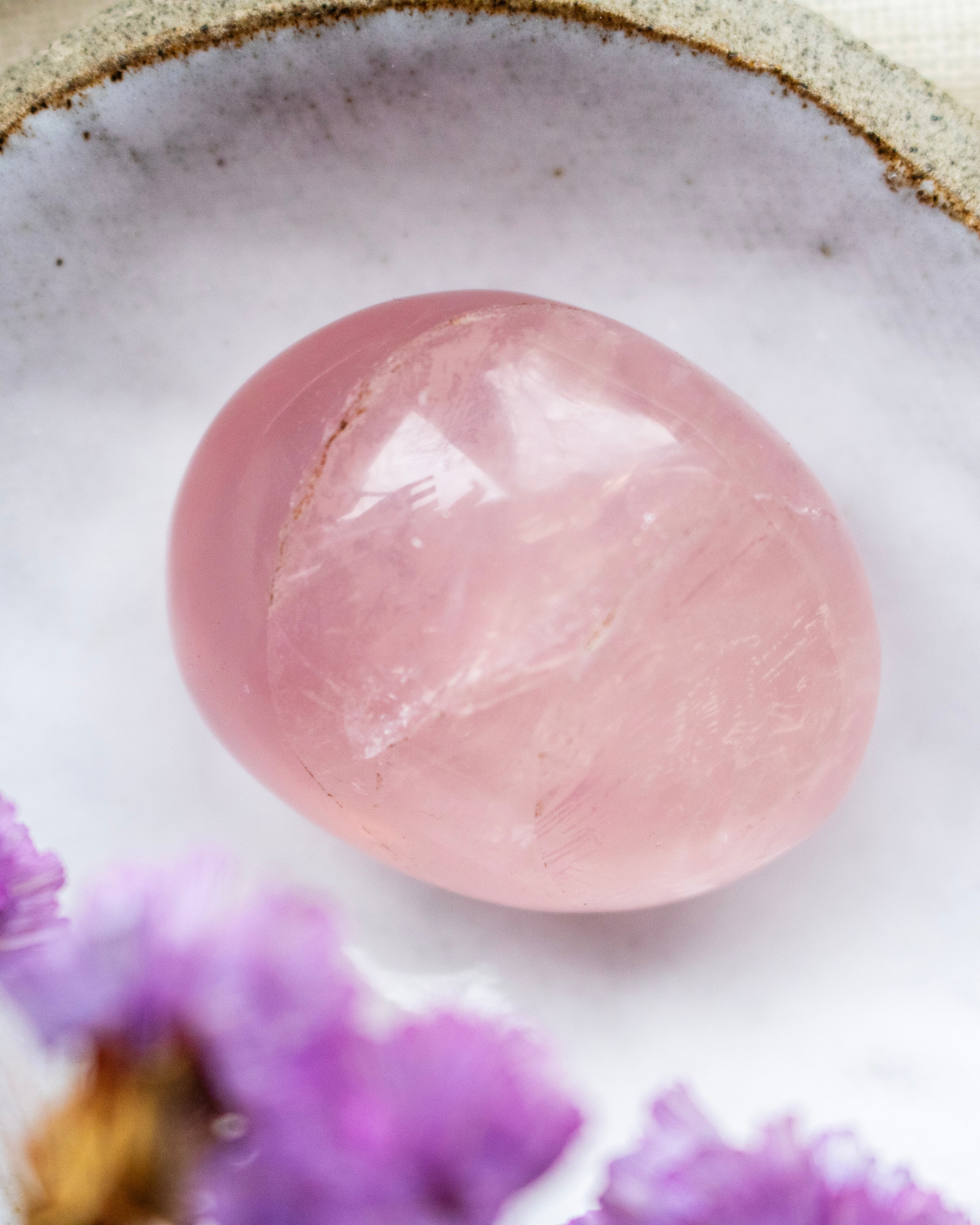 Pink crystal ball on a white surface with purple flowers in the background