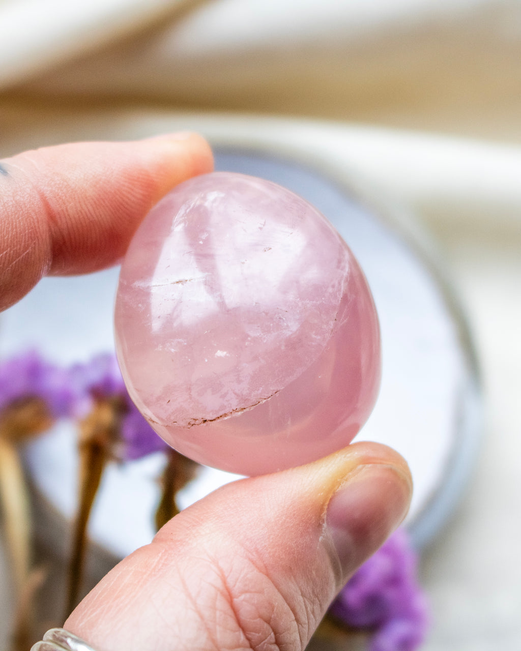 Hand holding a pink crystal ball with blurred purple flowers in the background