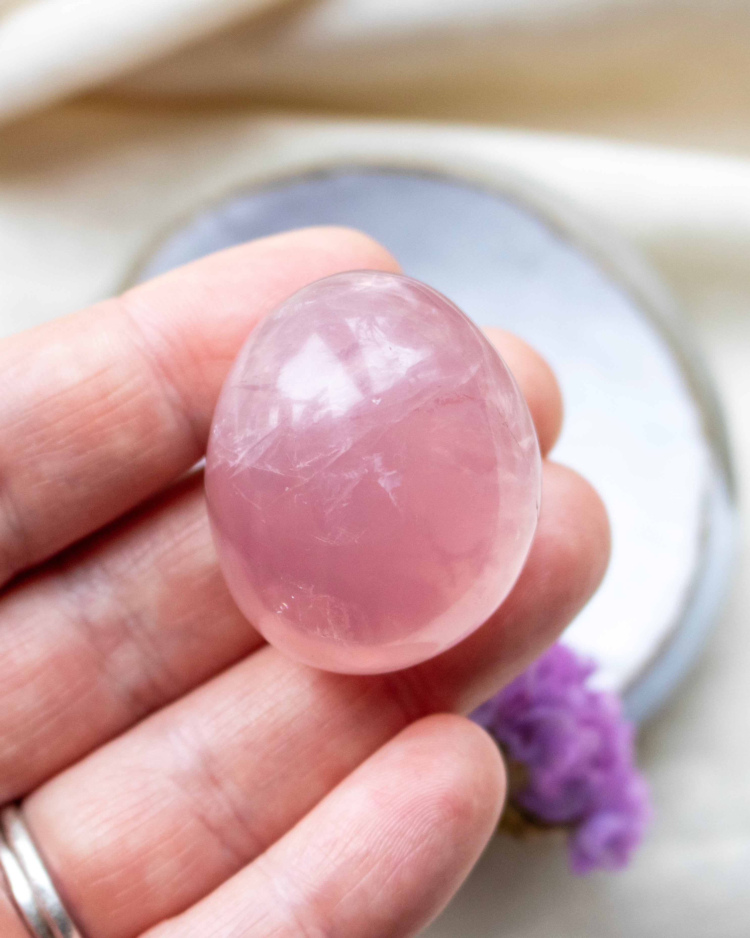 Pink crystal held in a hand with a blurred background