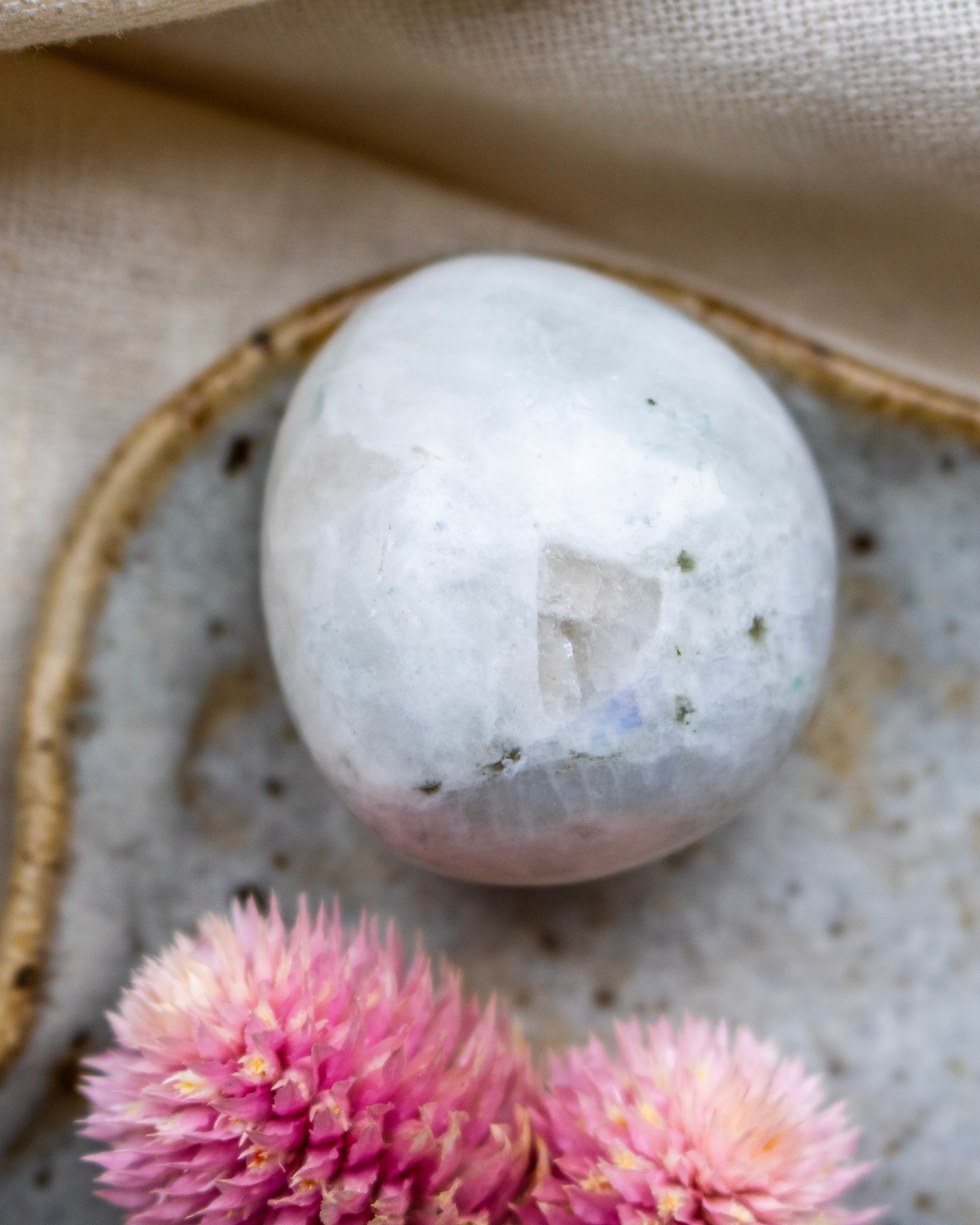 Round stone on a textured surface with pink flowers in the foreground