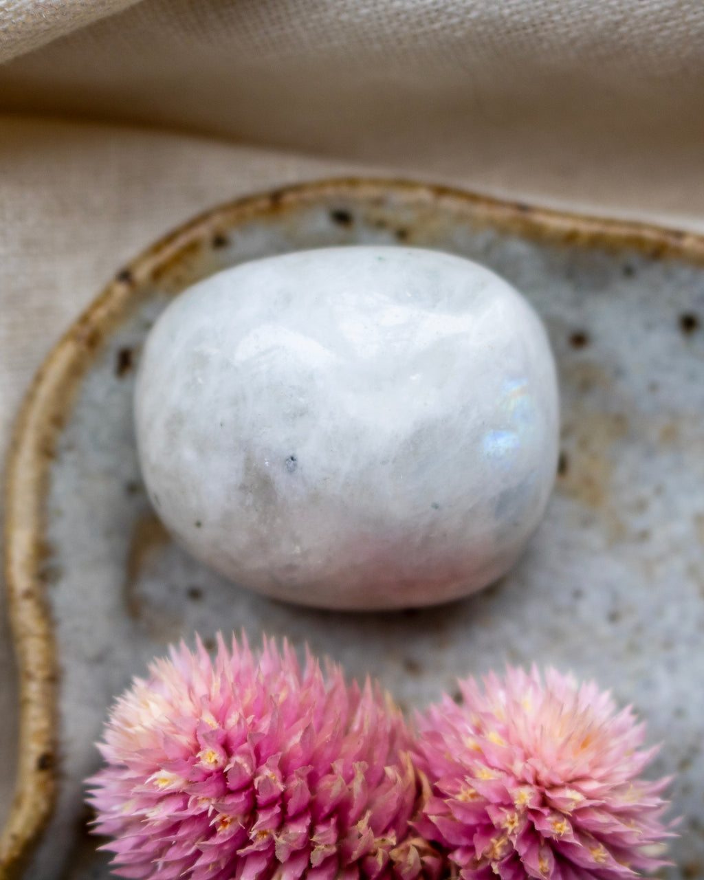 White stone on a textured surface with pink flowers in the foreground