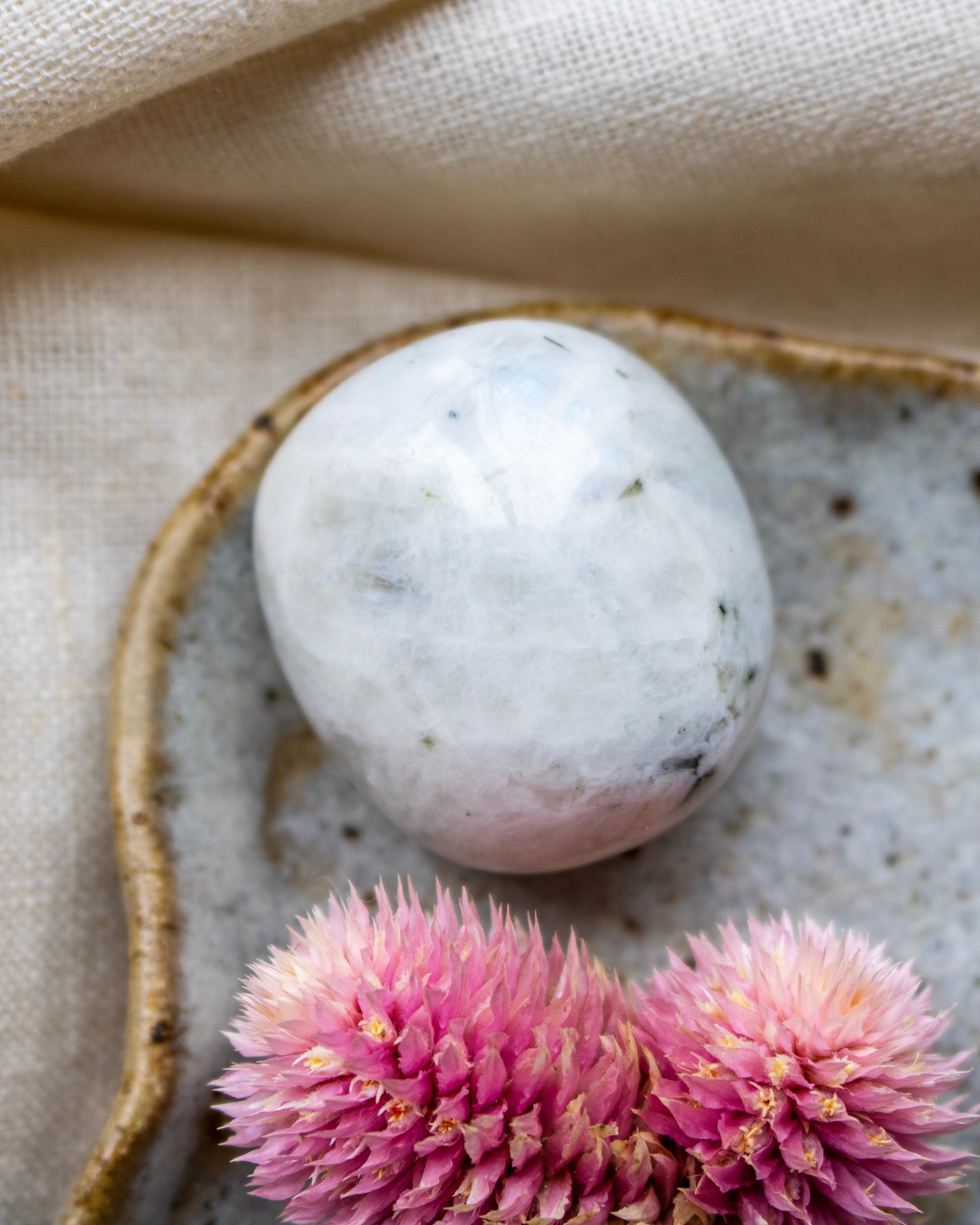 White marble sphere on a textured ceramic plate with pink flowers on a beige fabric background