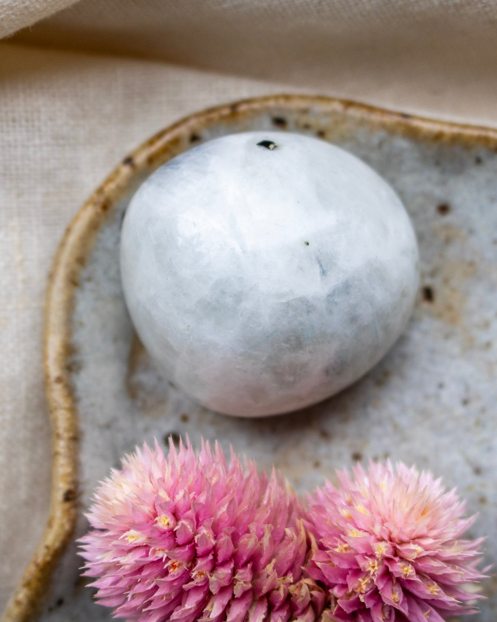 White marble sphere on a textured surface with pink flowers in the foreground