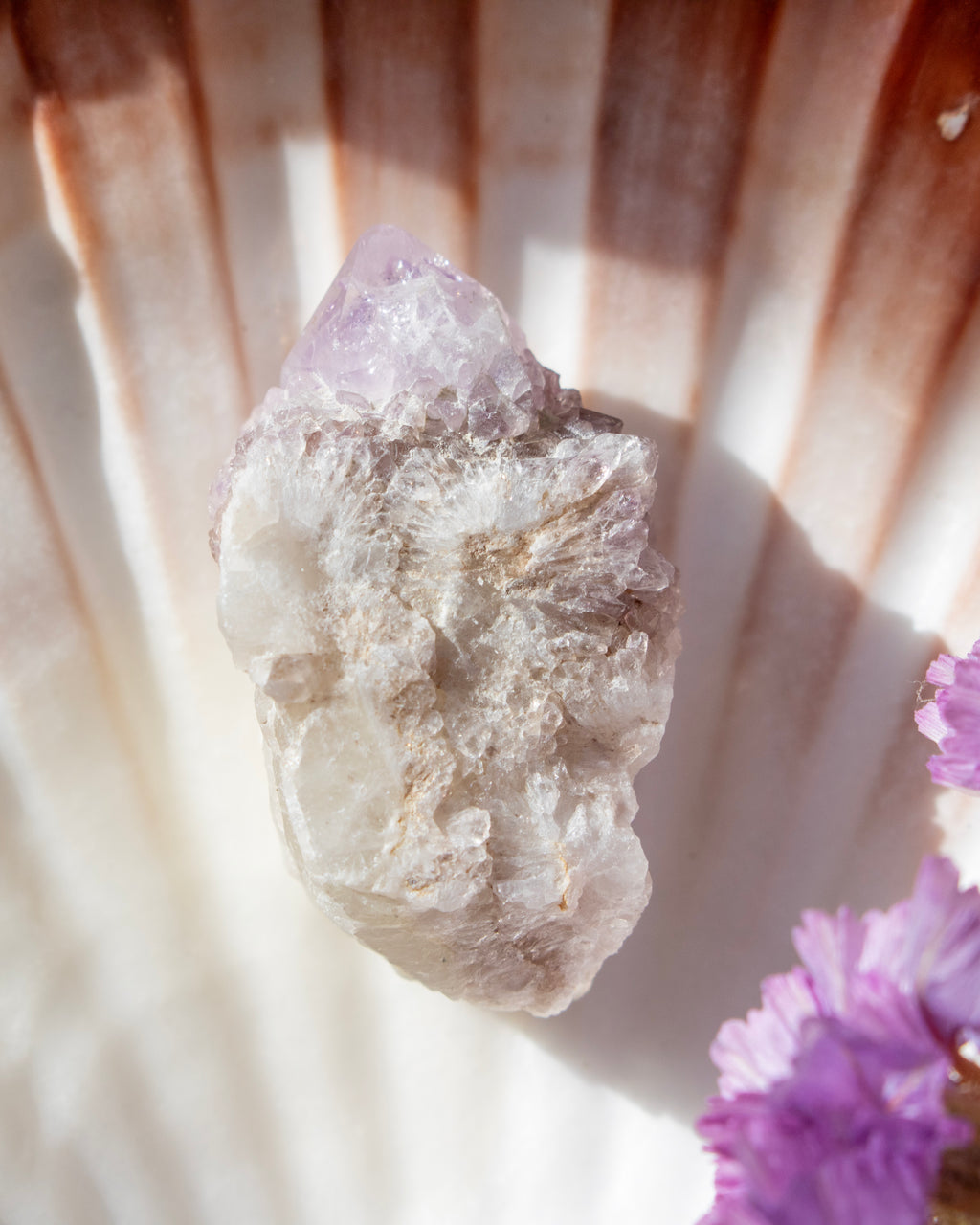 Crystal rock with a purple crystal on top, surrounded by purple flowers, on a textured surface.