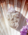 Crystal rock with a purple crystal on top, surrounded by purple flowers, on a textured surface.
