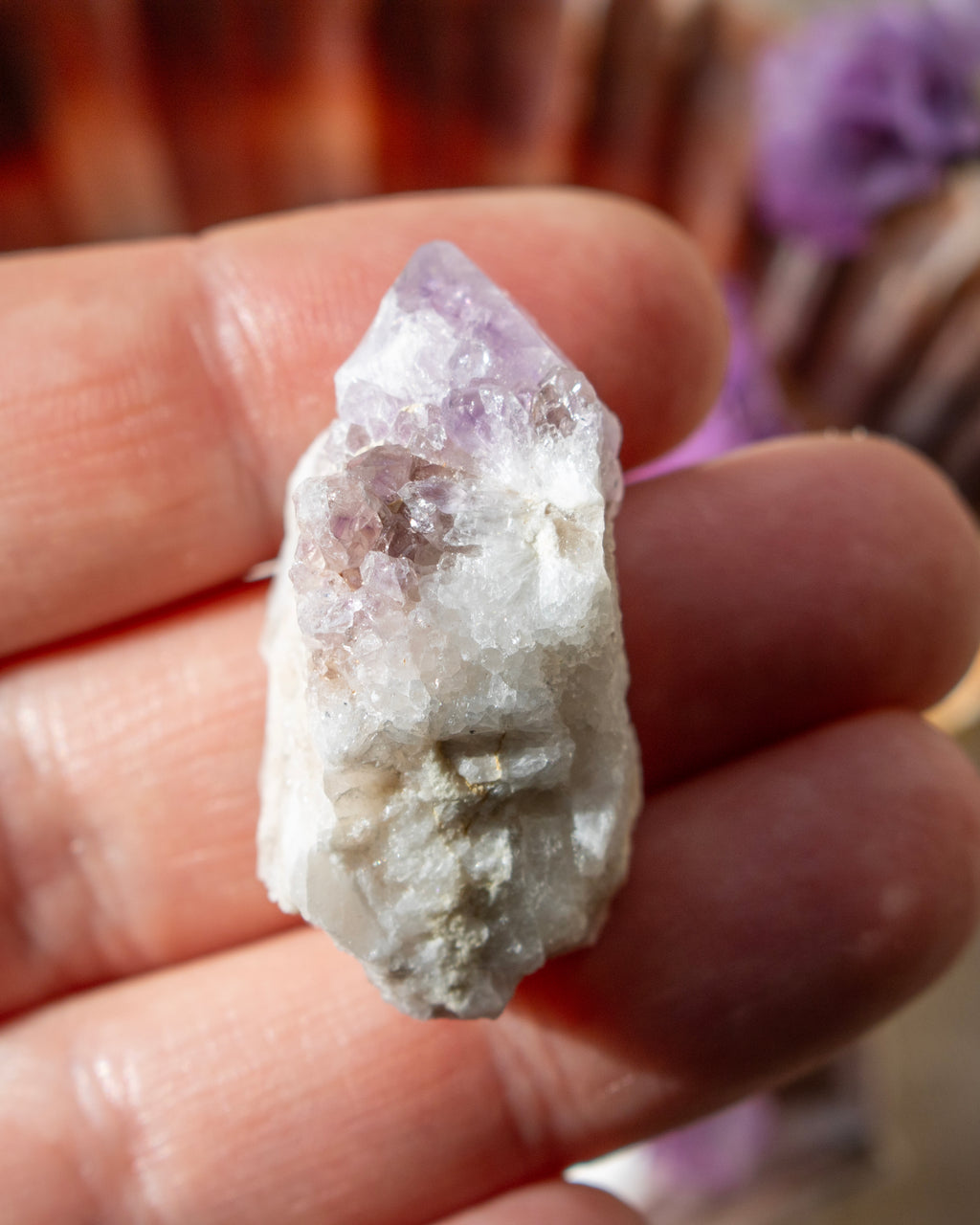 Amethyst crystal held between fingers with a blurred background