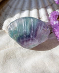 Translucent shell with purple and green hues on a textured surface with pink flowers.