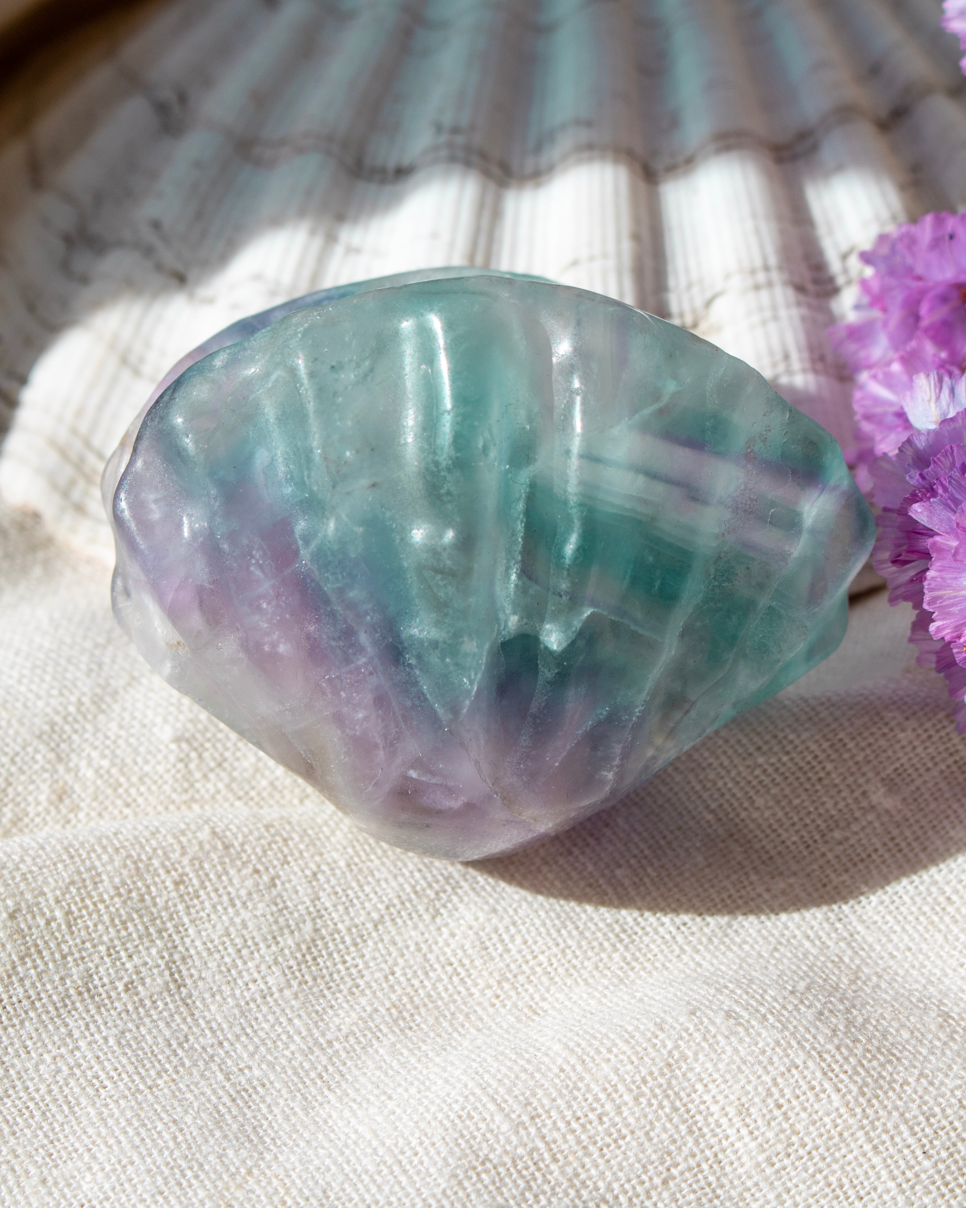 Crystal rock with purple and green hues on a textured surface with pink flowers.