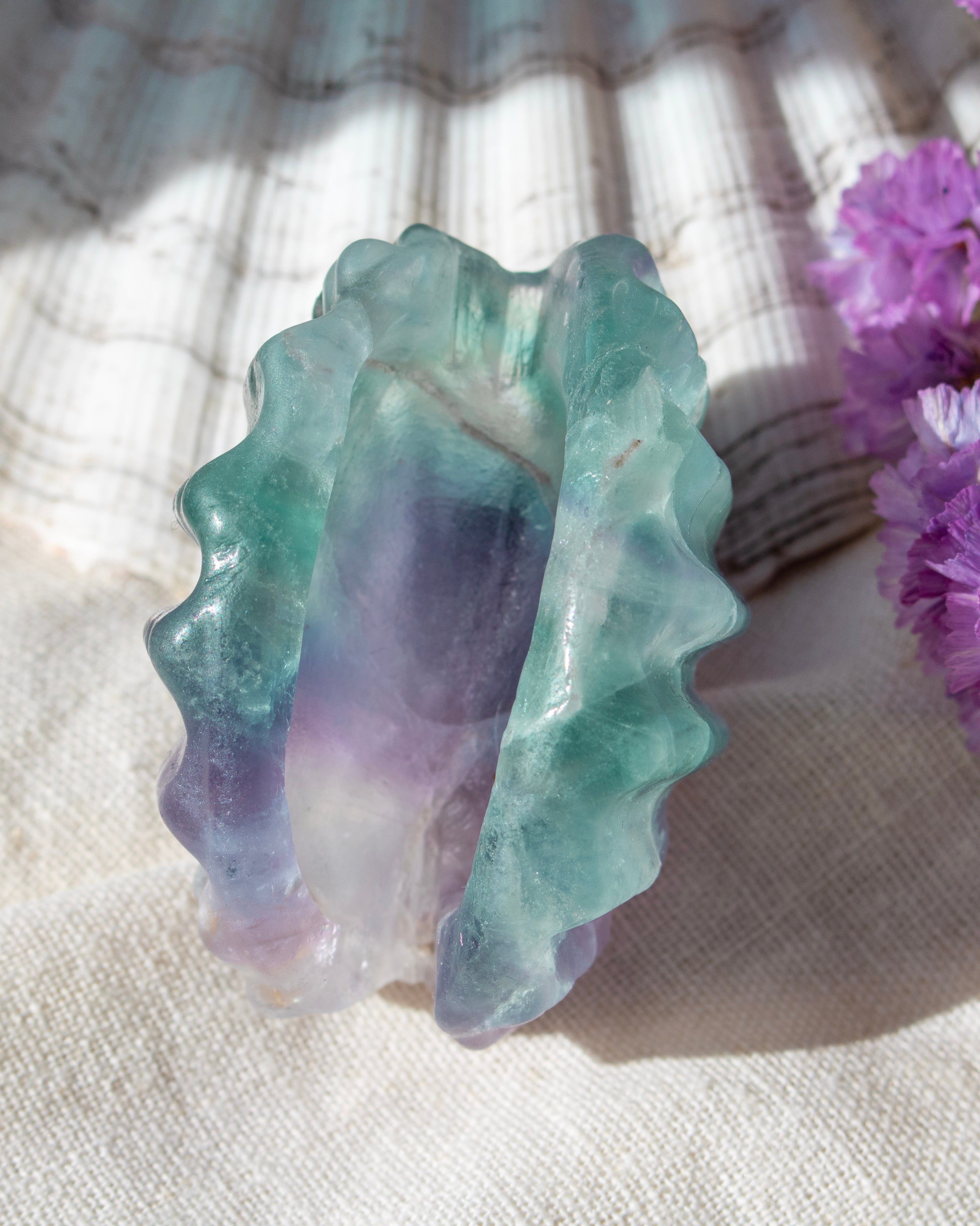 Multicolored stone with wavy texture on a textured surface with purple flowers.