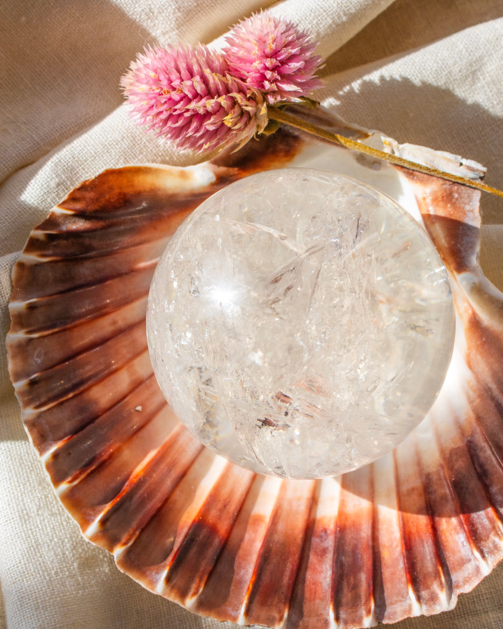 Crystal ball on a seashell with pink flowers and a beige cloth background