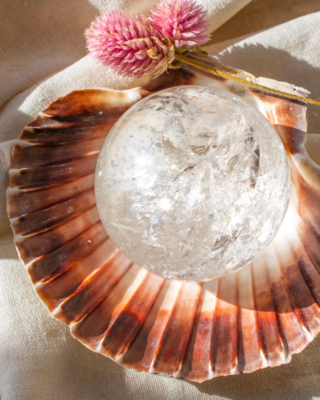 Crystal ball on a large shell with a pink flower and gold leaf on a beige fabric background