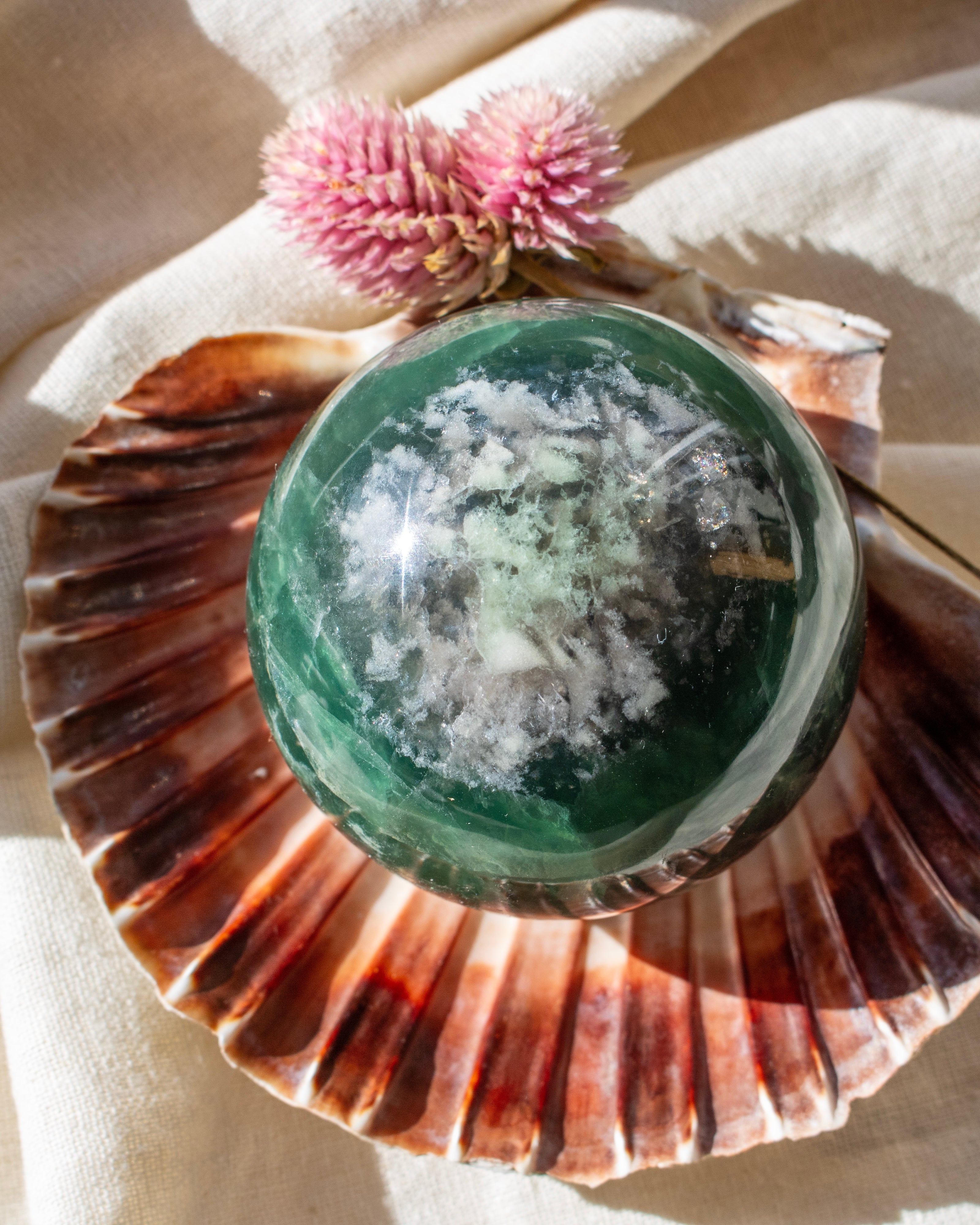 Green crystal ball inside a seashell with pink flowers on a beige background