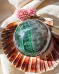 Green crystal ball inside a seashell with a pink flower in the background
