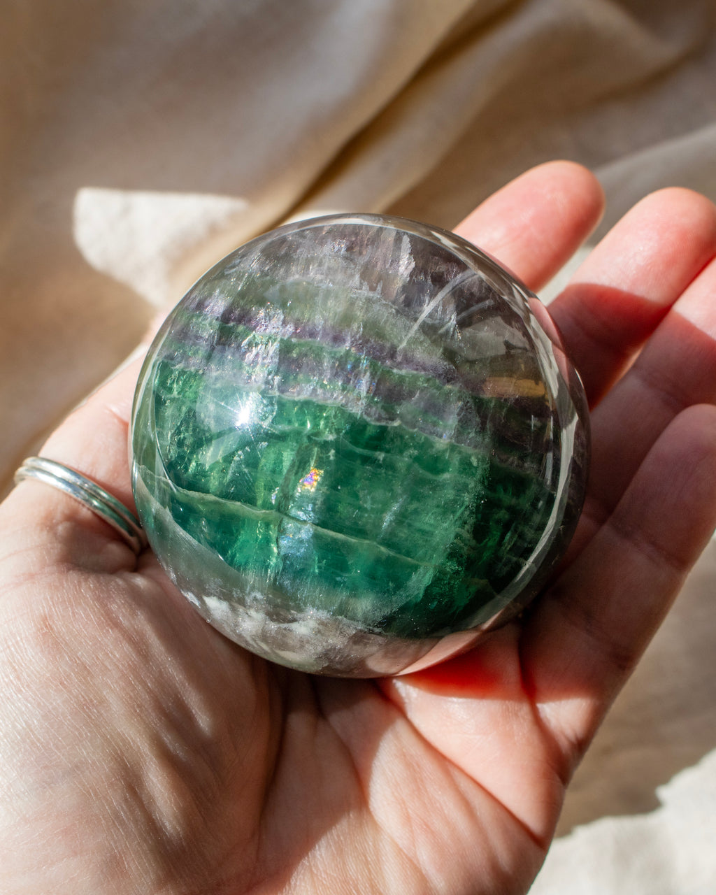 Hand holding a green crystal ball with a blurred beige background