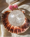 Seashell with a crystal ball and pink flower on a beige fabric background