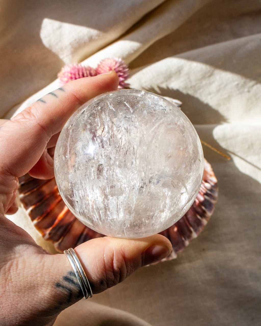 Hand holding a clear crystal sphere with a shell and fabric in the background