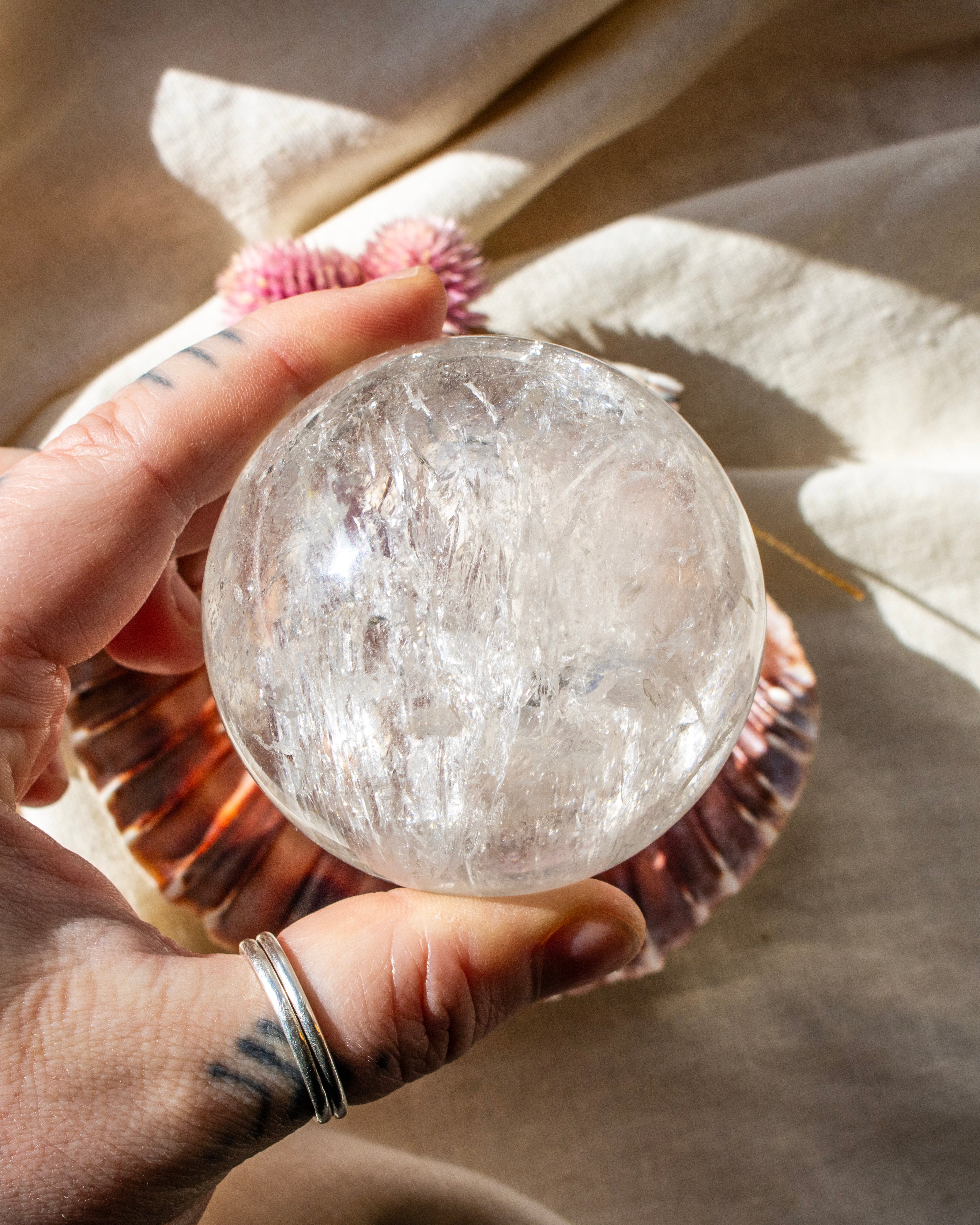 Hand holding a clear crystal sphere with a shell and fabric in the background
