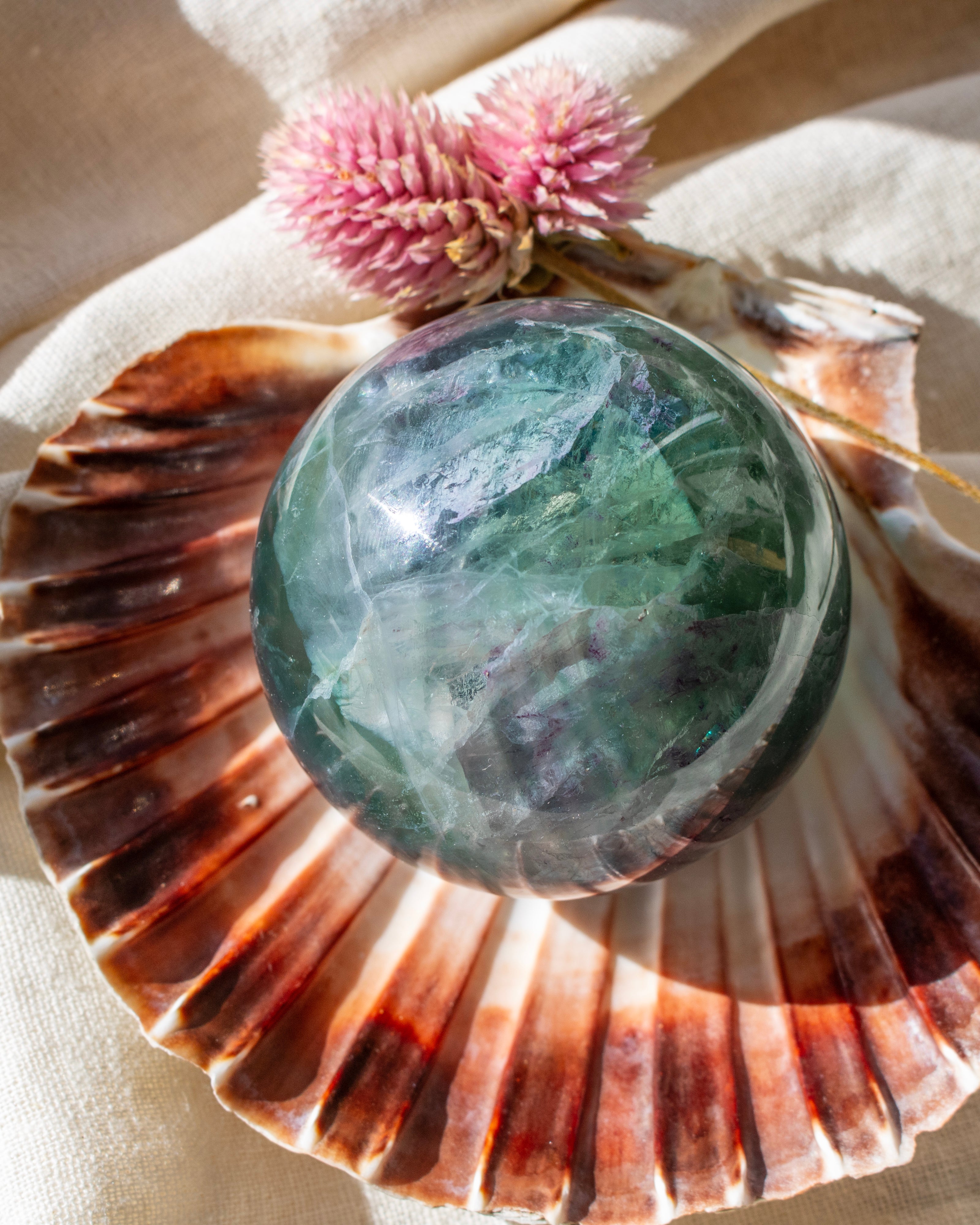 Green crystal ball on a large shell with pink flower in the background