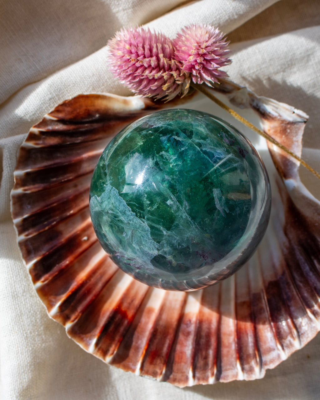 Green crystal ball on a large shell with pink flowers in the background
