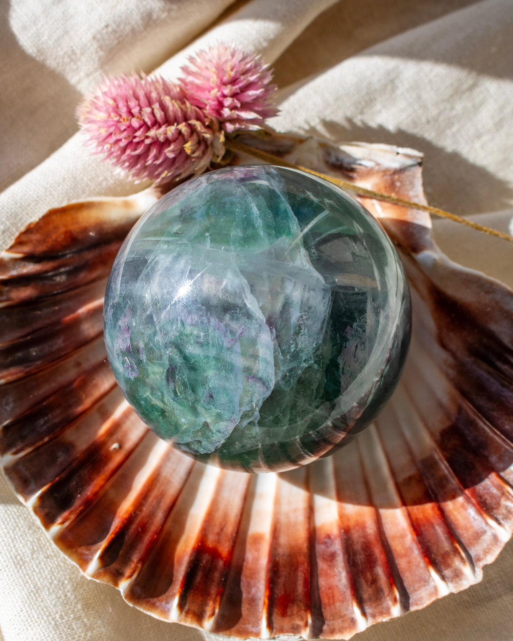 Crystal ball on a large shell with pink flowers in the background