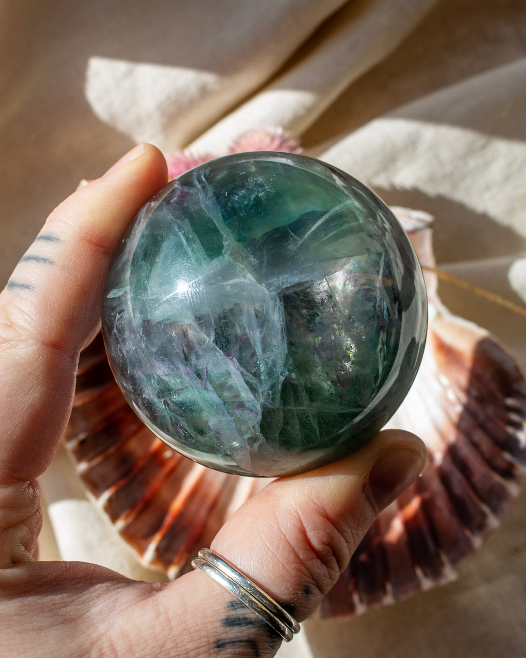 Hand holding a green crystal ball with a shell in the background