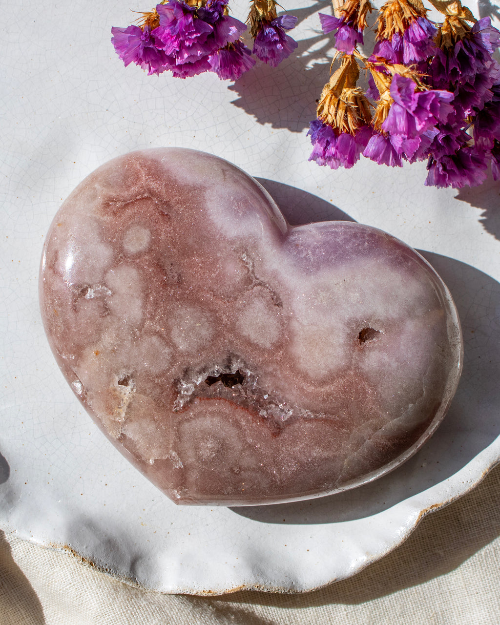 Heart-shaped purple stone on a light surface with purple flowers in the background