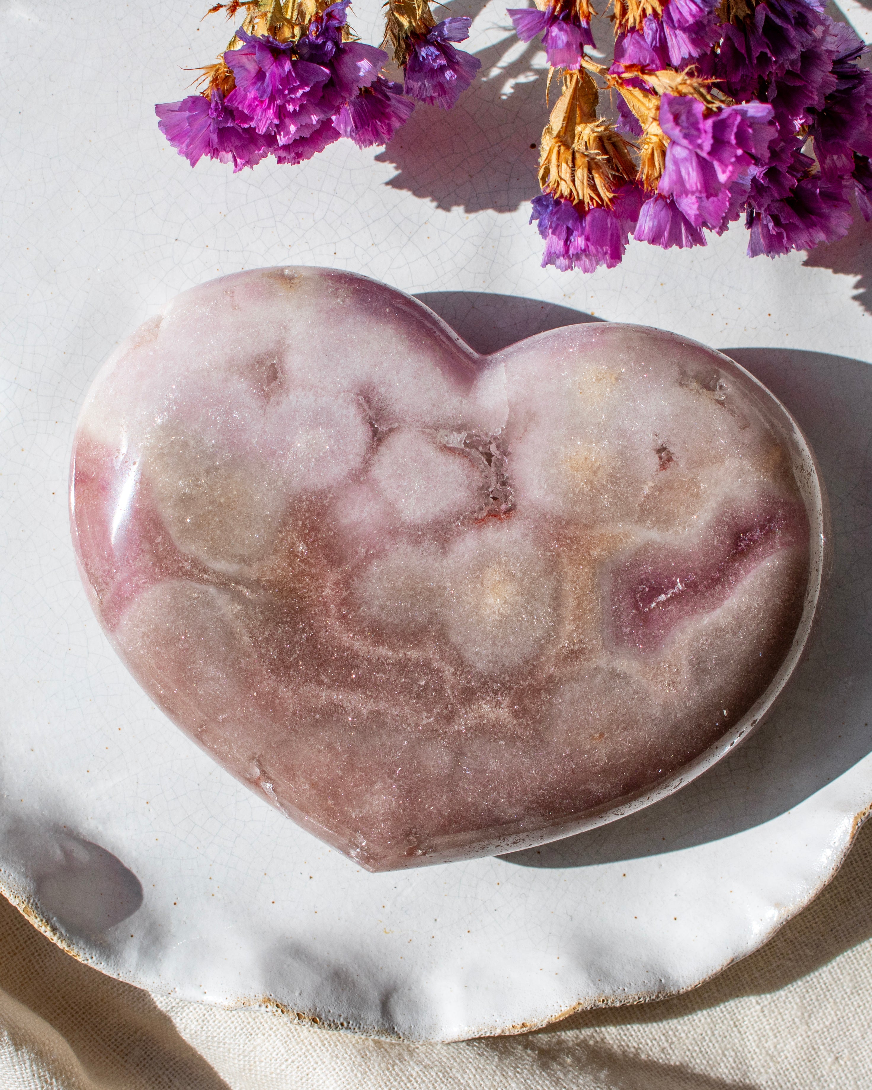 Heart-shaped purple stone on a white surface with purple flowers in the background