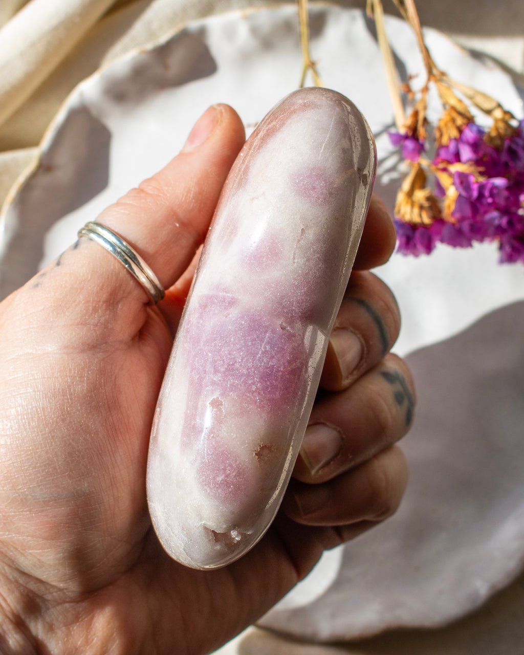 Hand holding a pink crystal with a blurred background of flowers and fabric