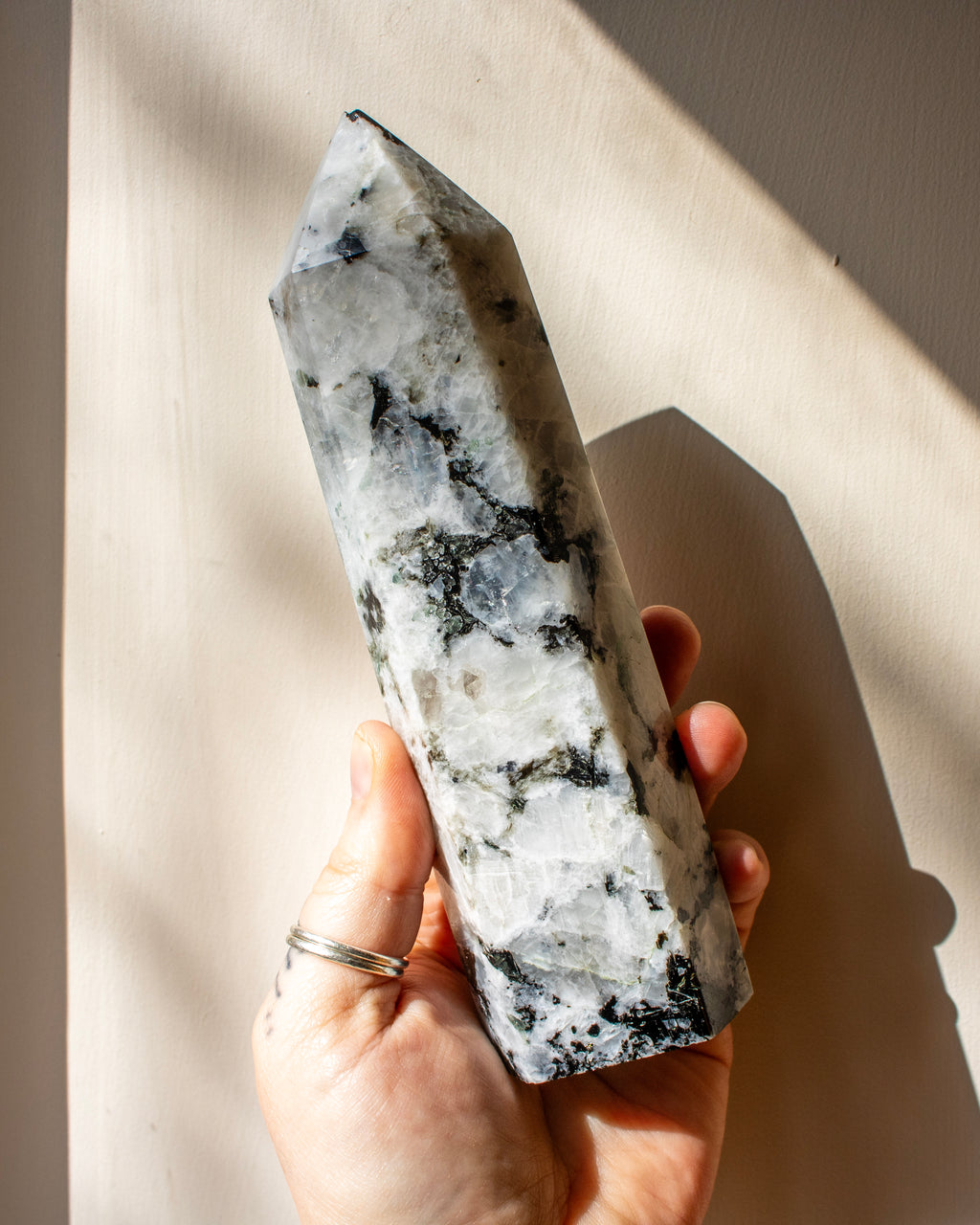 Hand holding a large crystal with a white and gray pattern against a neutral background