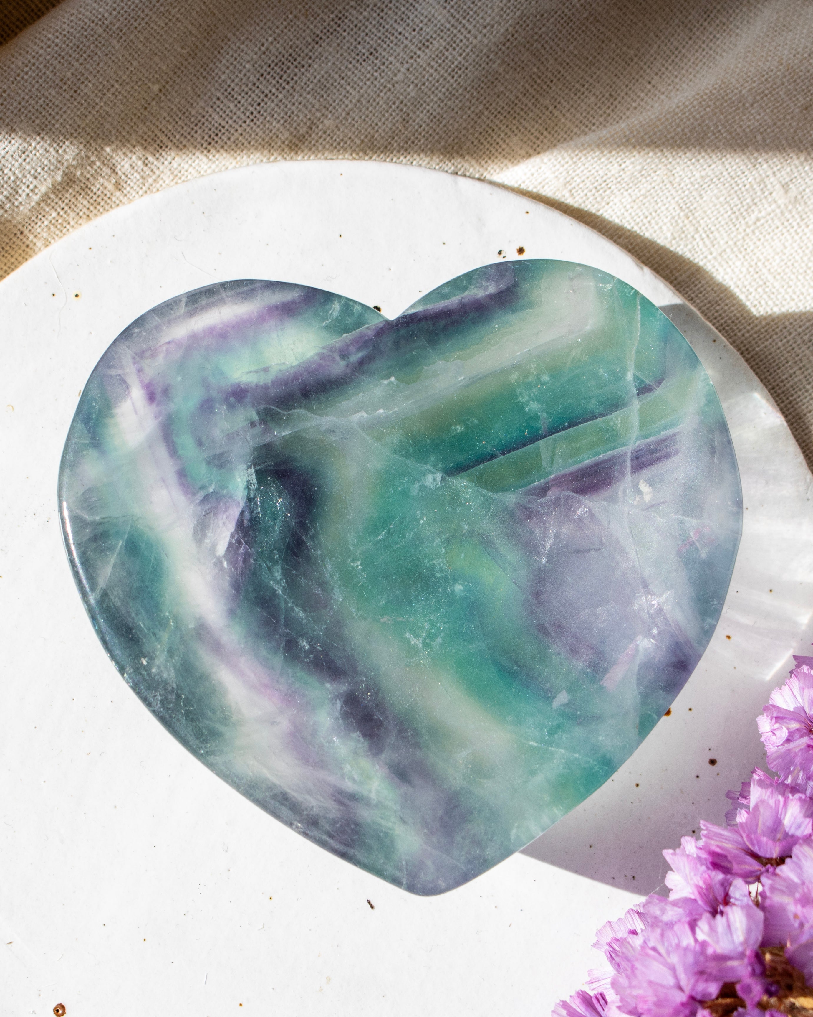 Heart-shaped green and purple stone on a white plate with a blurred background