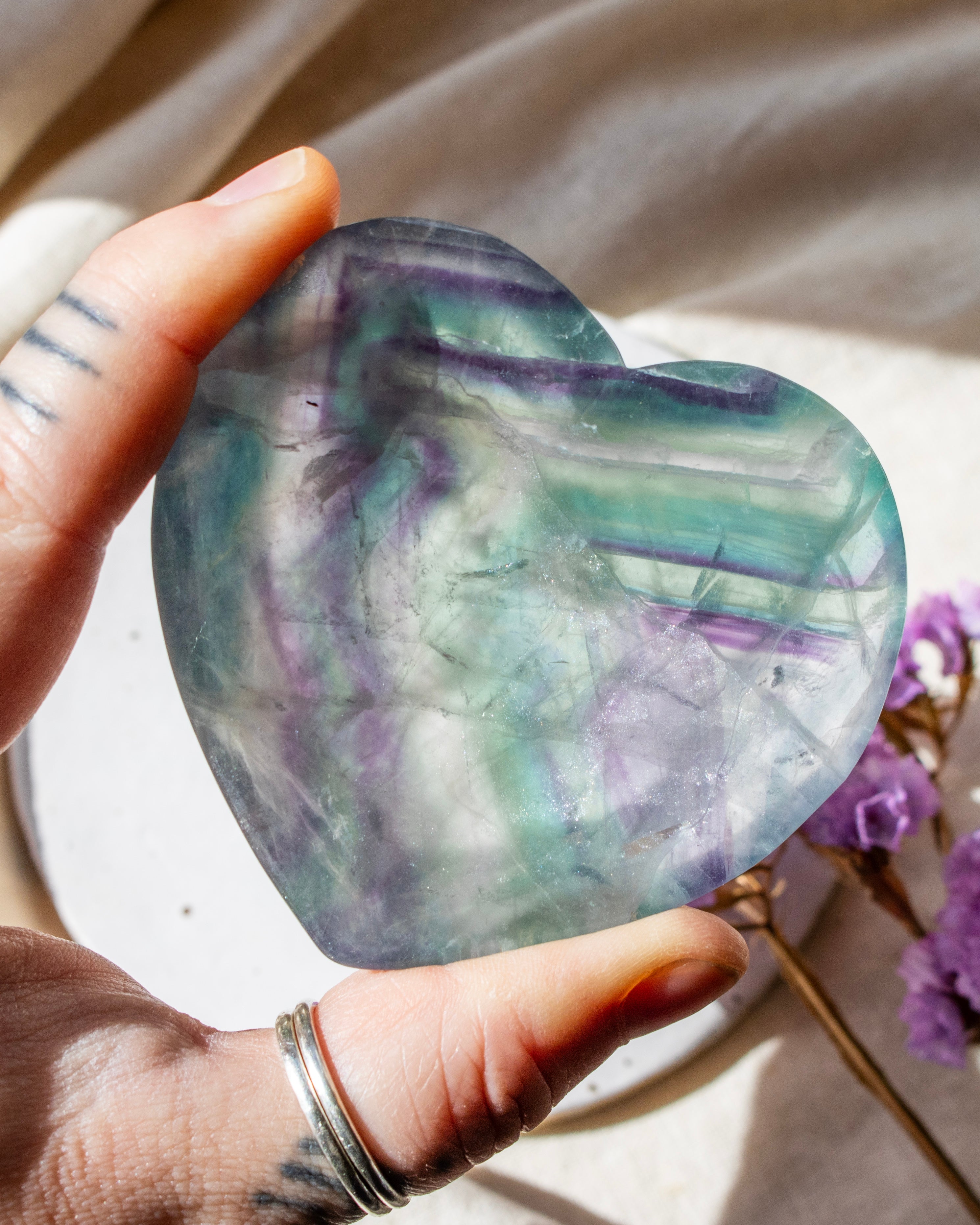 Heart-shaped multicolored crystal held by a hand with a ring, against a neutral background.