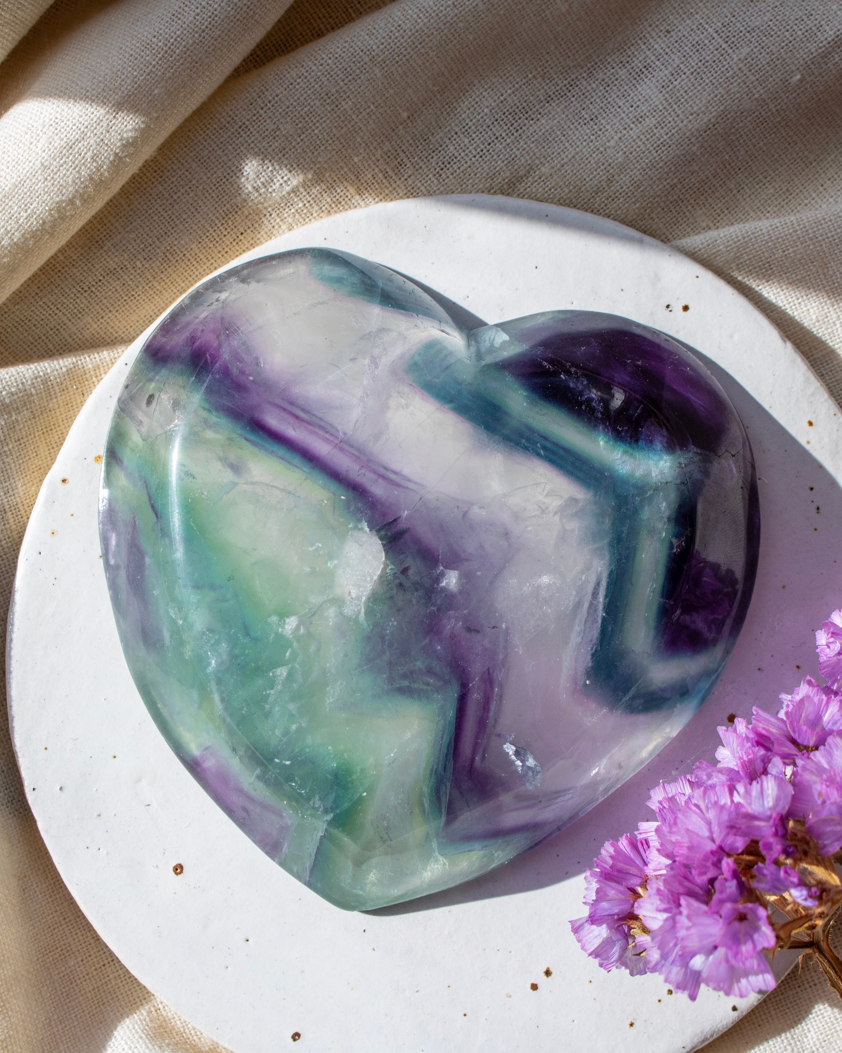 Heart-shaped purple and green soap on a white plate with a beige fabric background