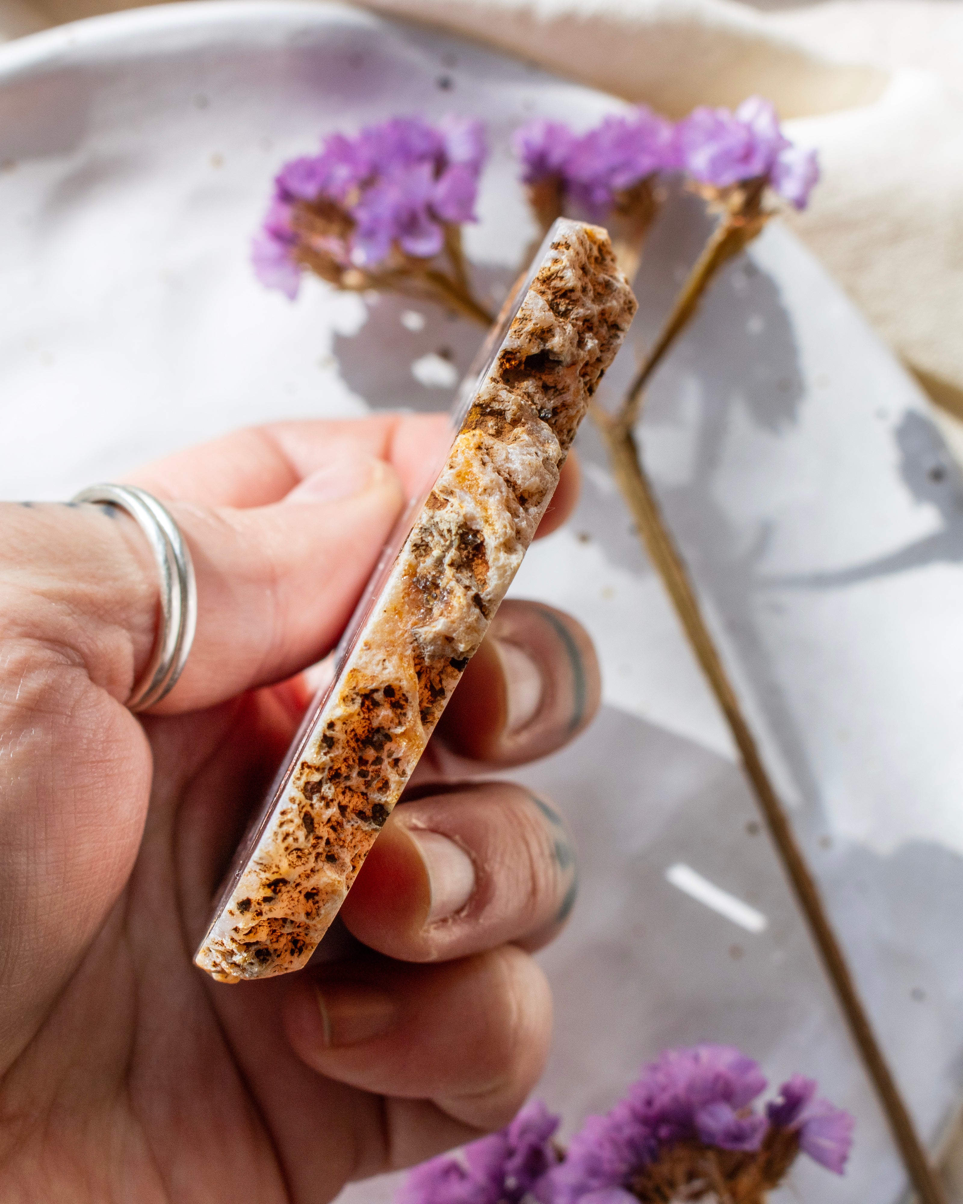 Hand holding a textured object with purple flowers in the background