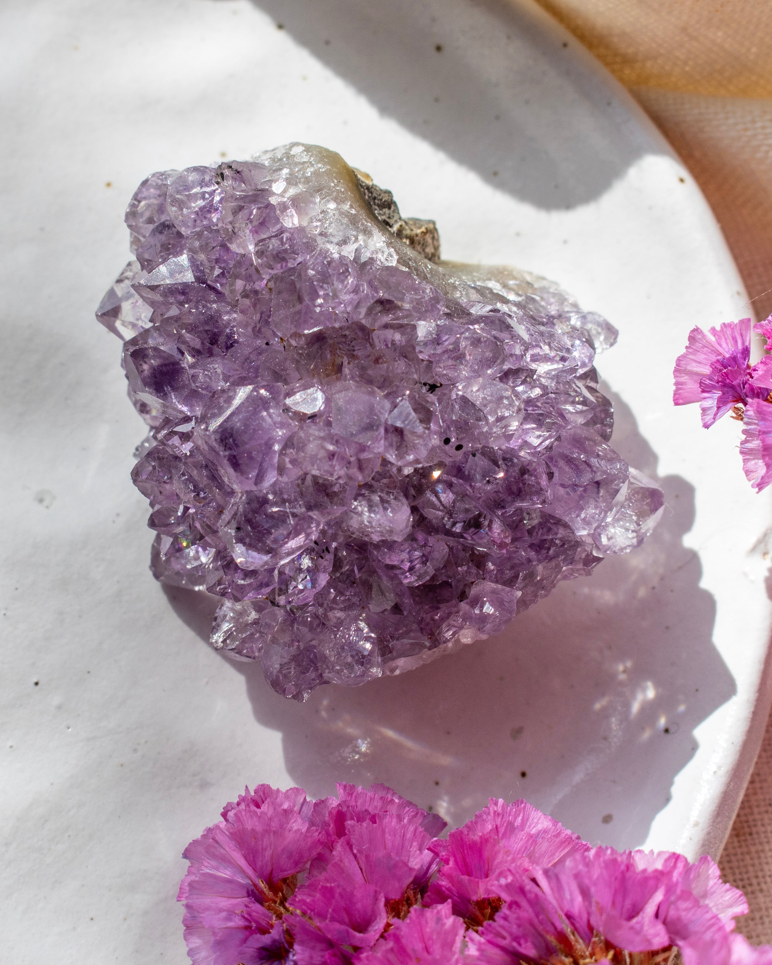 Amethyst crystal cluster on a white surface with pink flowers