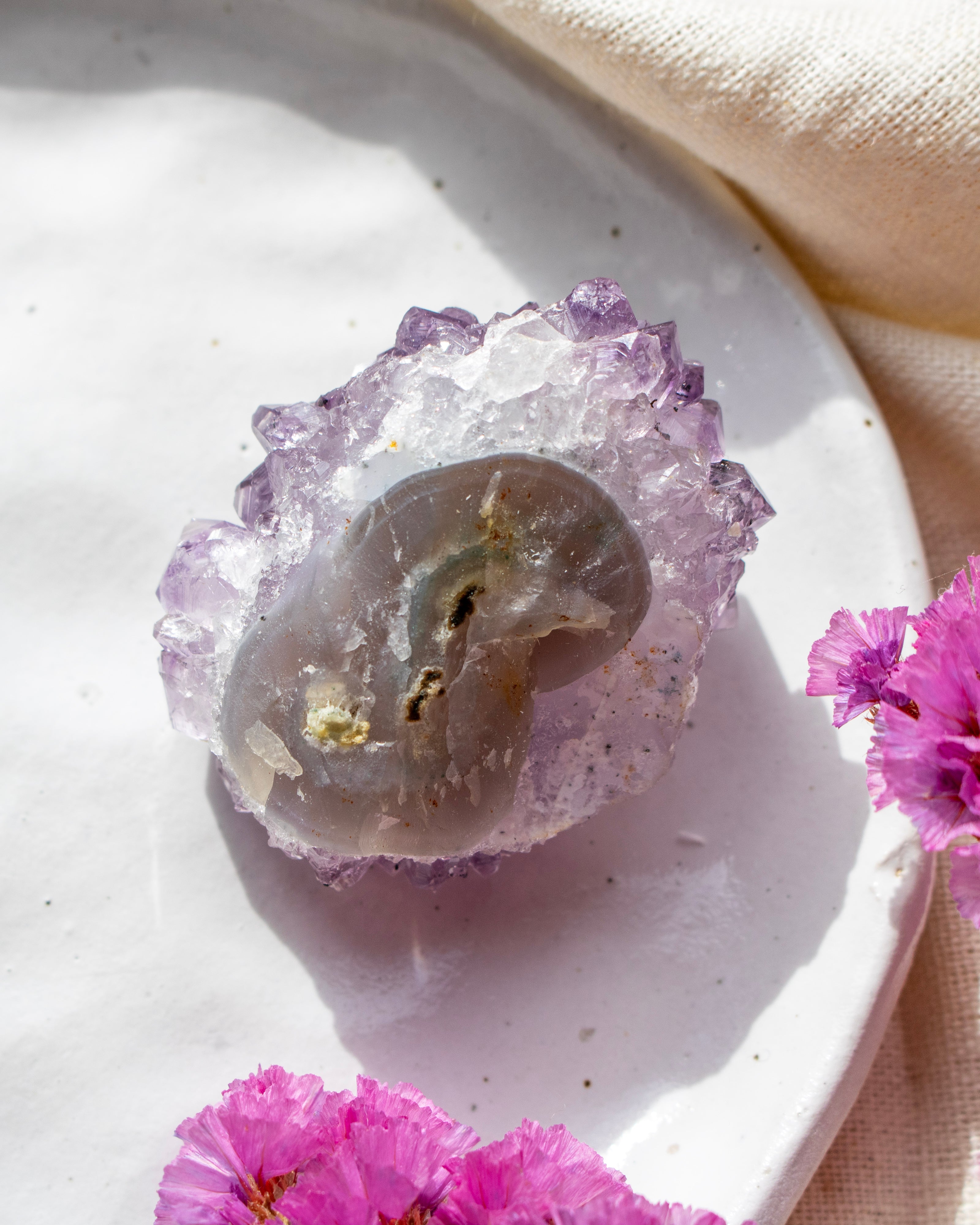 Amethyst crystal on a white stone with pink flowers