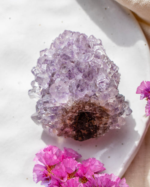 Amethyst crystal on a white plate with pink flowers
