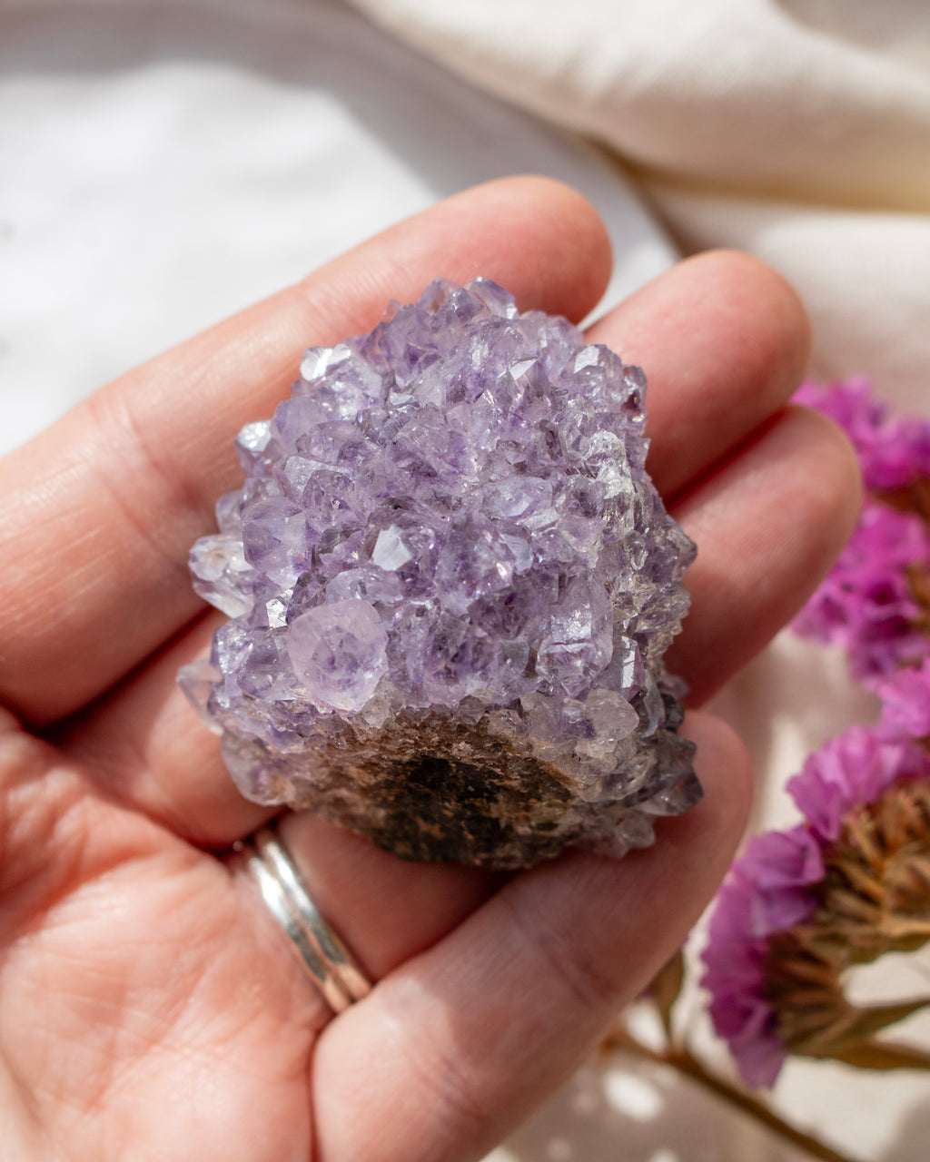 Hand holding a purple crystal with pink flowers in the background