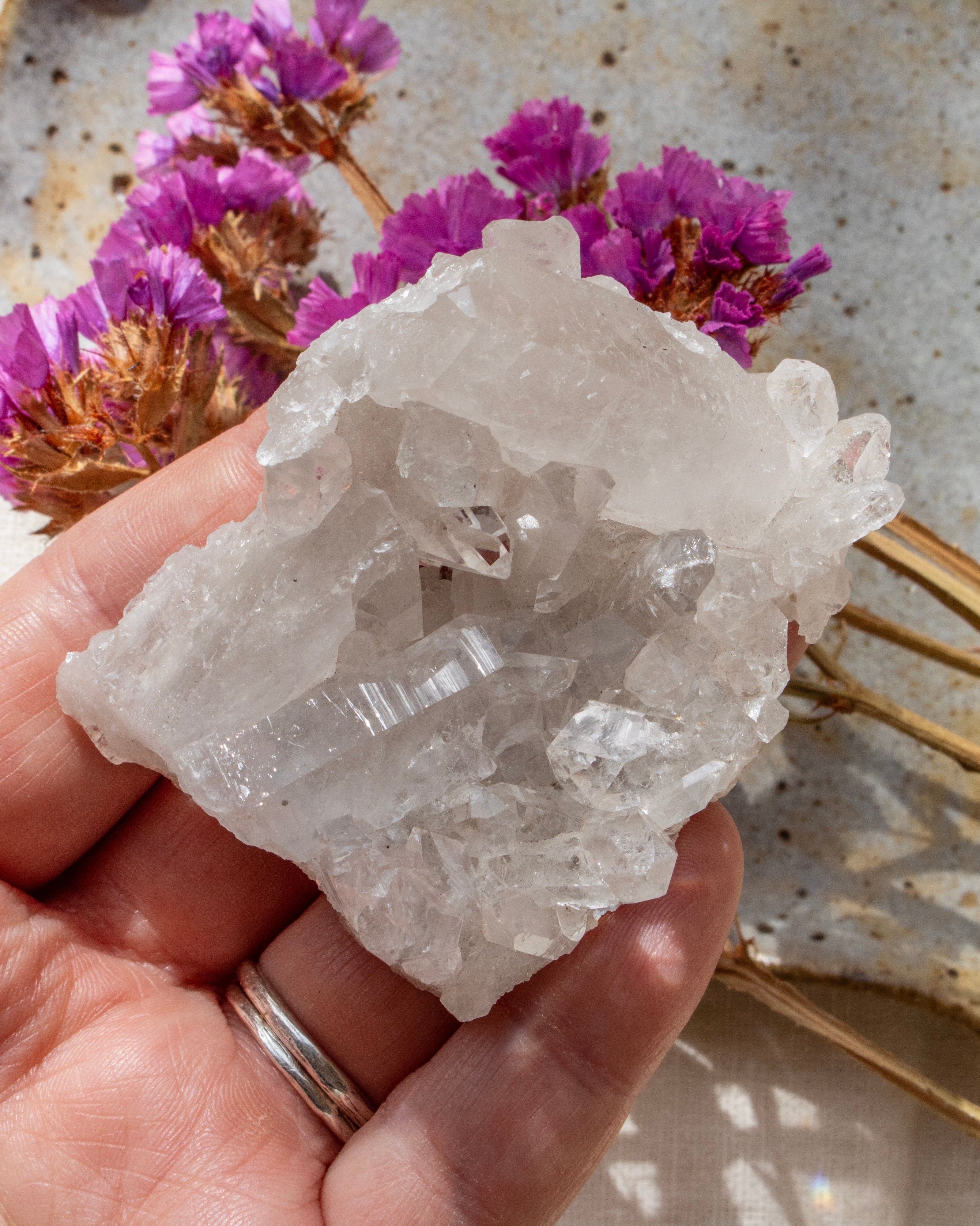 Crystal rock held by a hand with pink flowers in the background