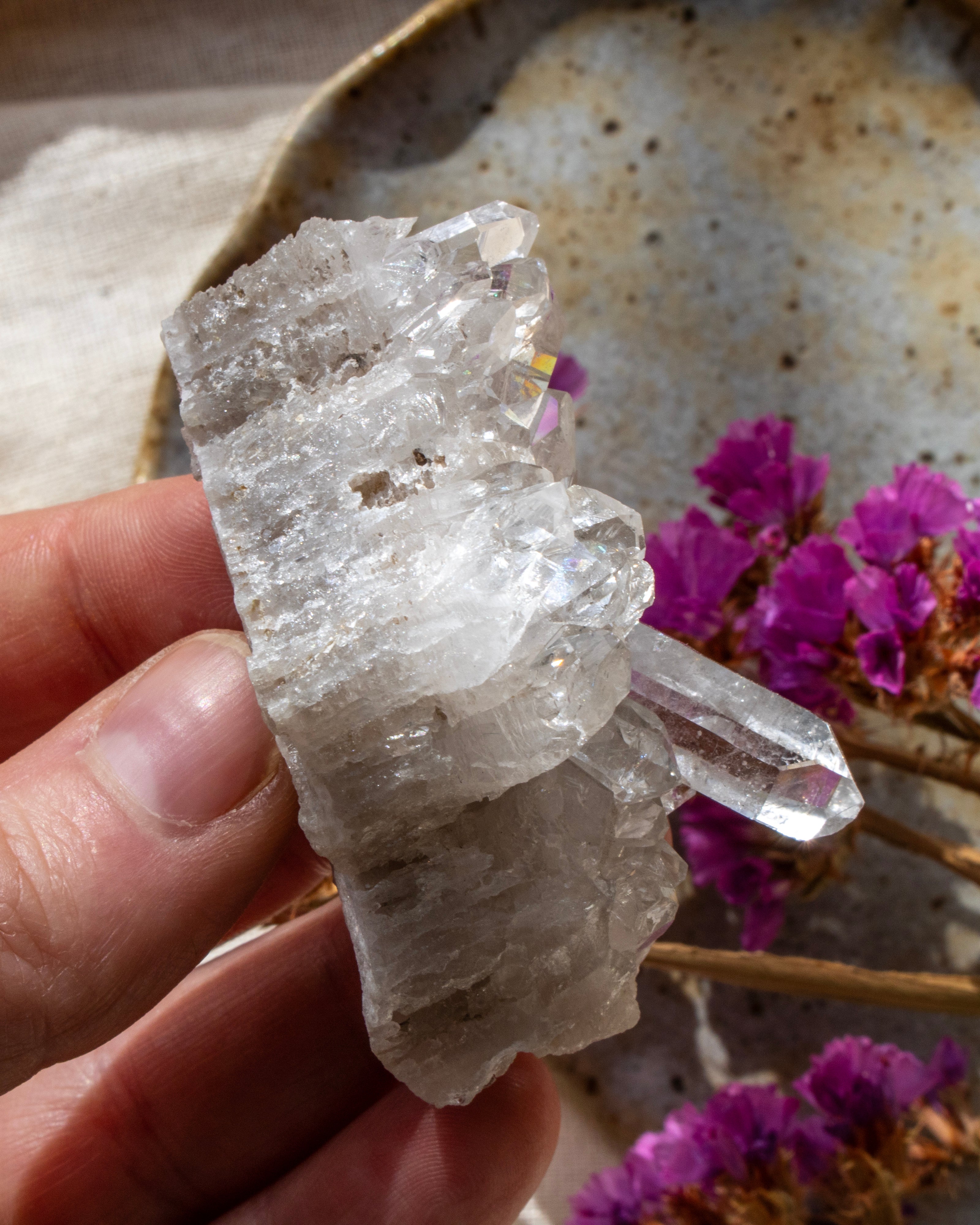 Clear crystal rock held by a hand with purple flowers in the background