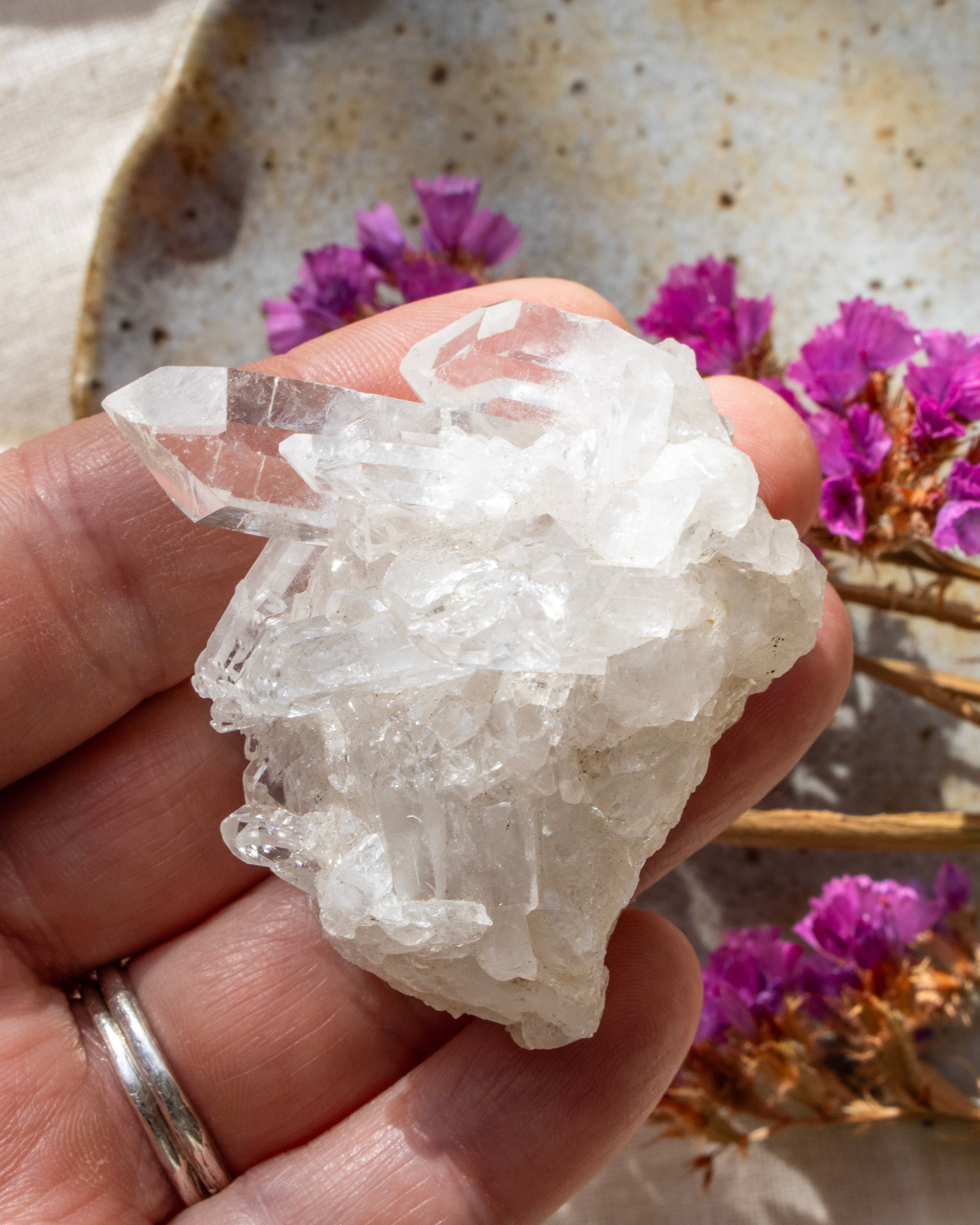 Clear crystal rock held in a hand with purple flowers in the background