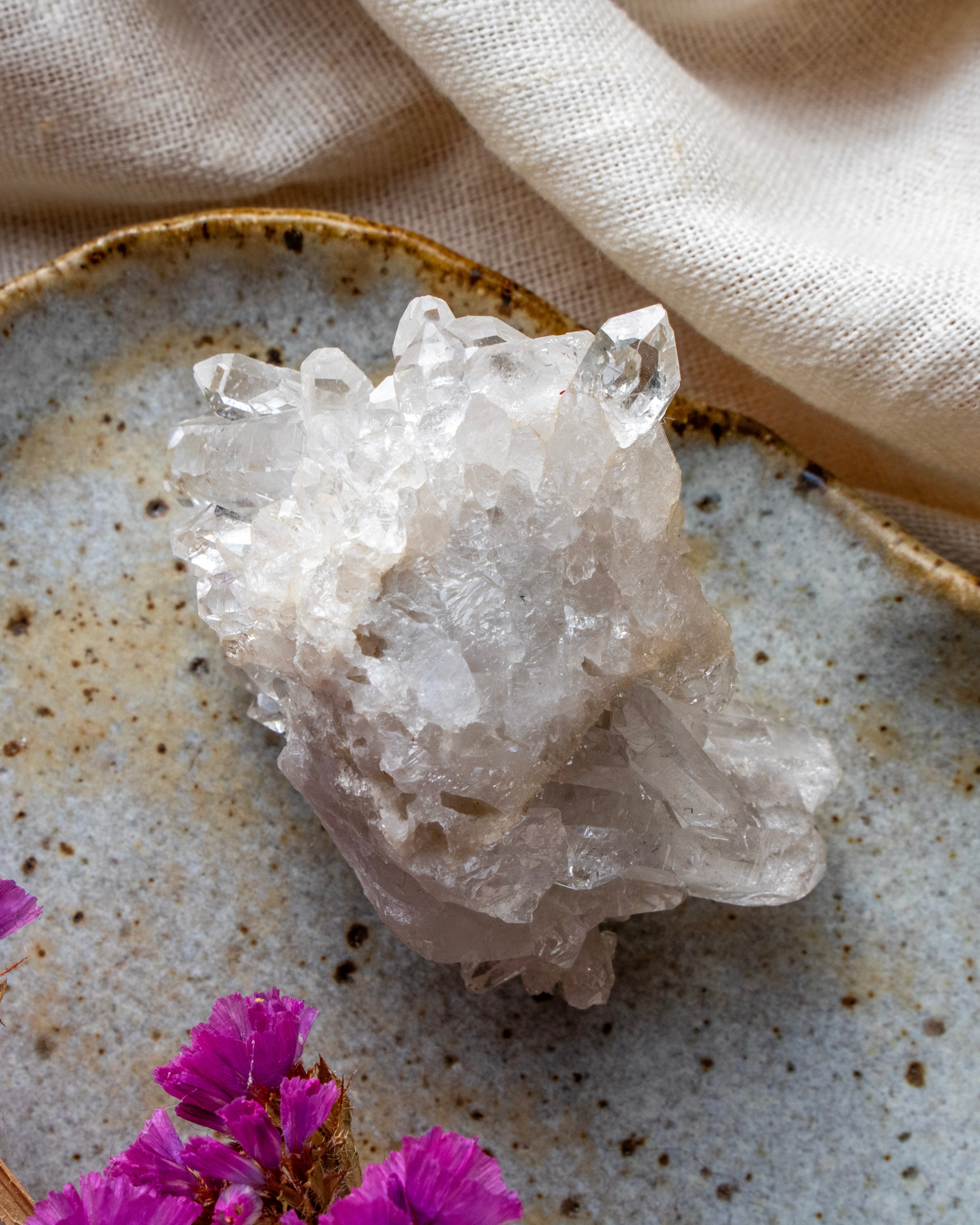 Crystal cluster on a textured surface with pink flowers and beige fabric