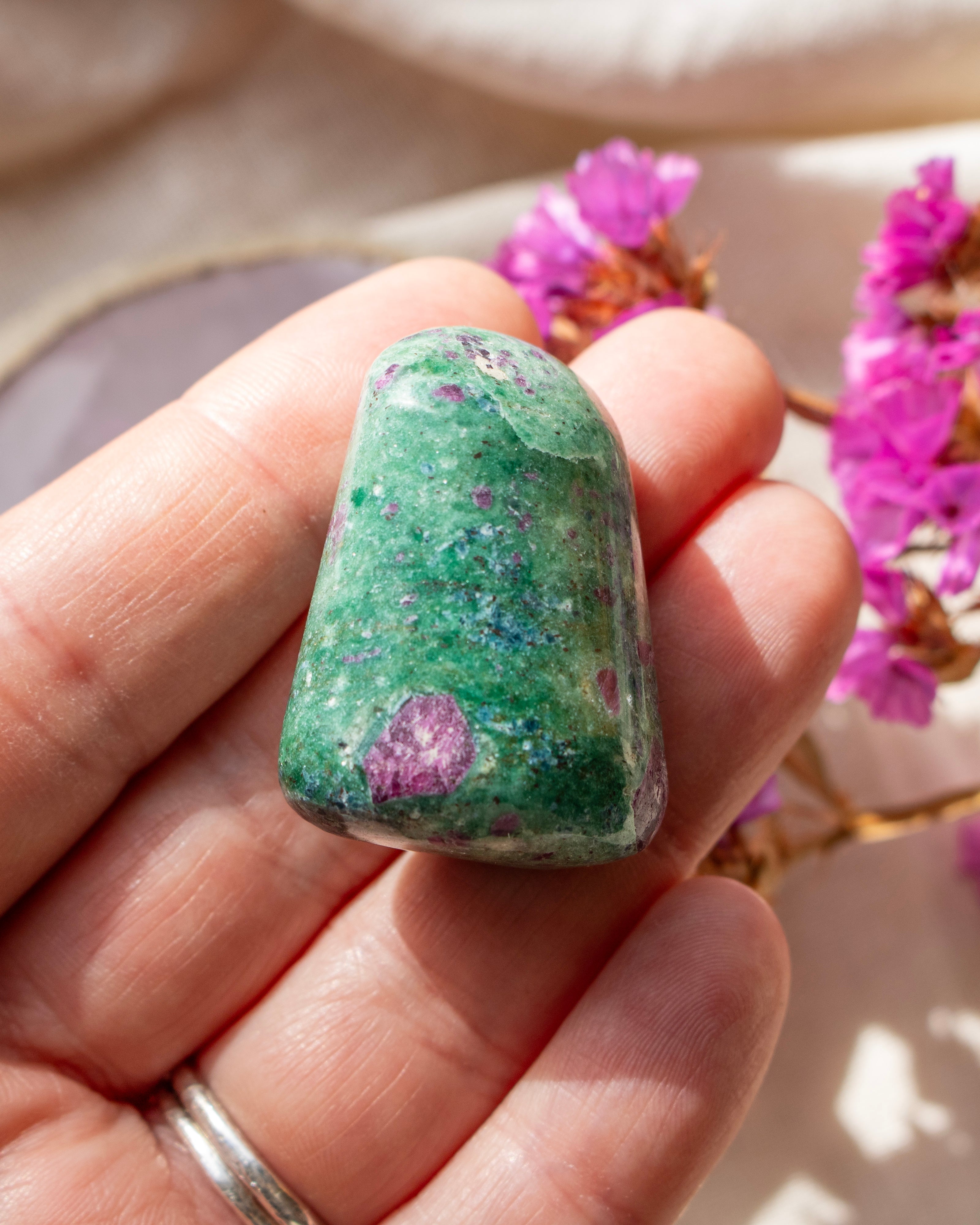 a green and purple stone being held on fingers with a blurred background